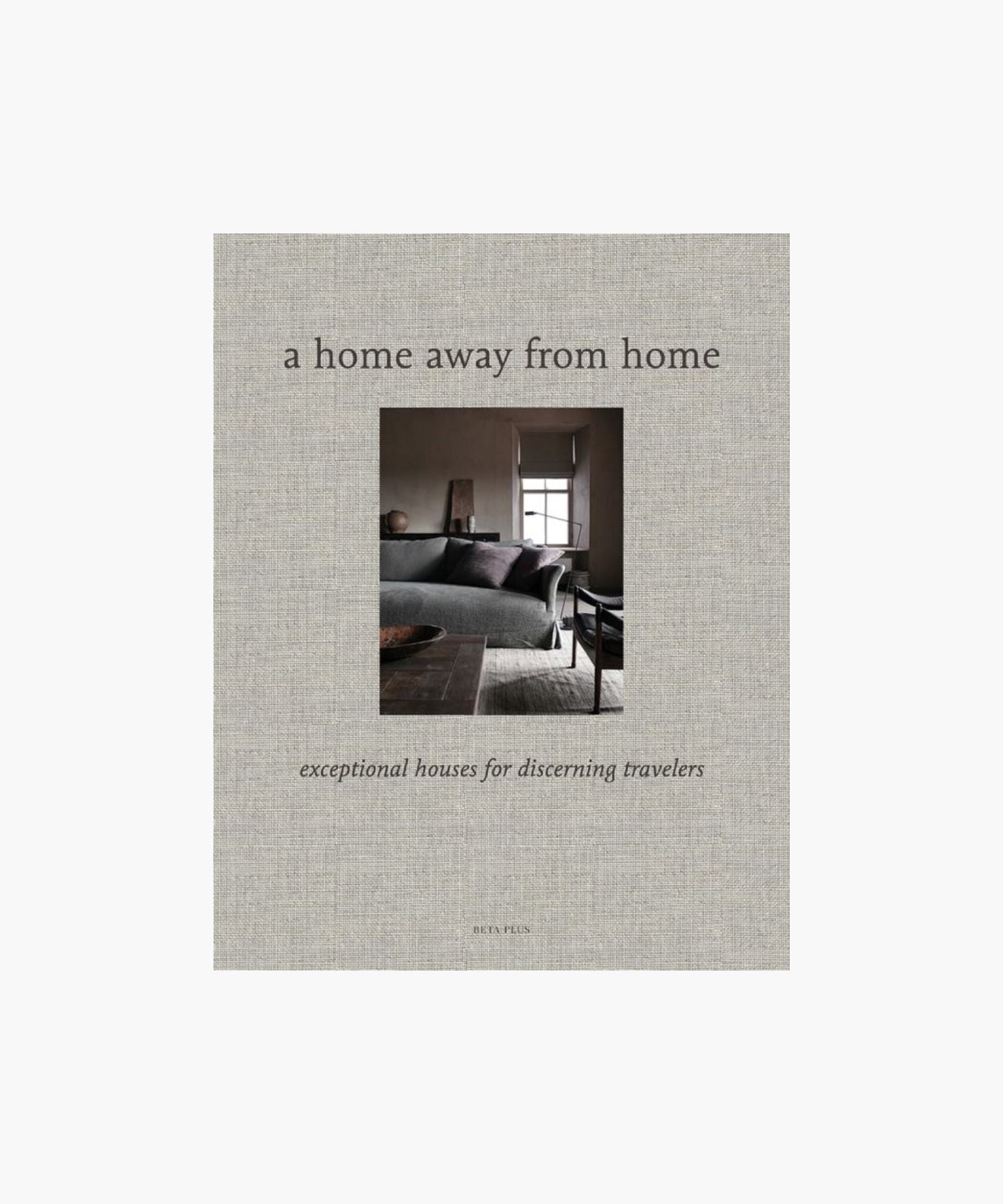 A cover of "A Home Away from Home" book; showcases a cozy, elegant living room with a gray sofa and large window, evoking warmth and sophistication. | Wildwood Home Co.