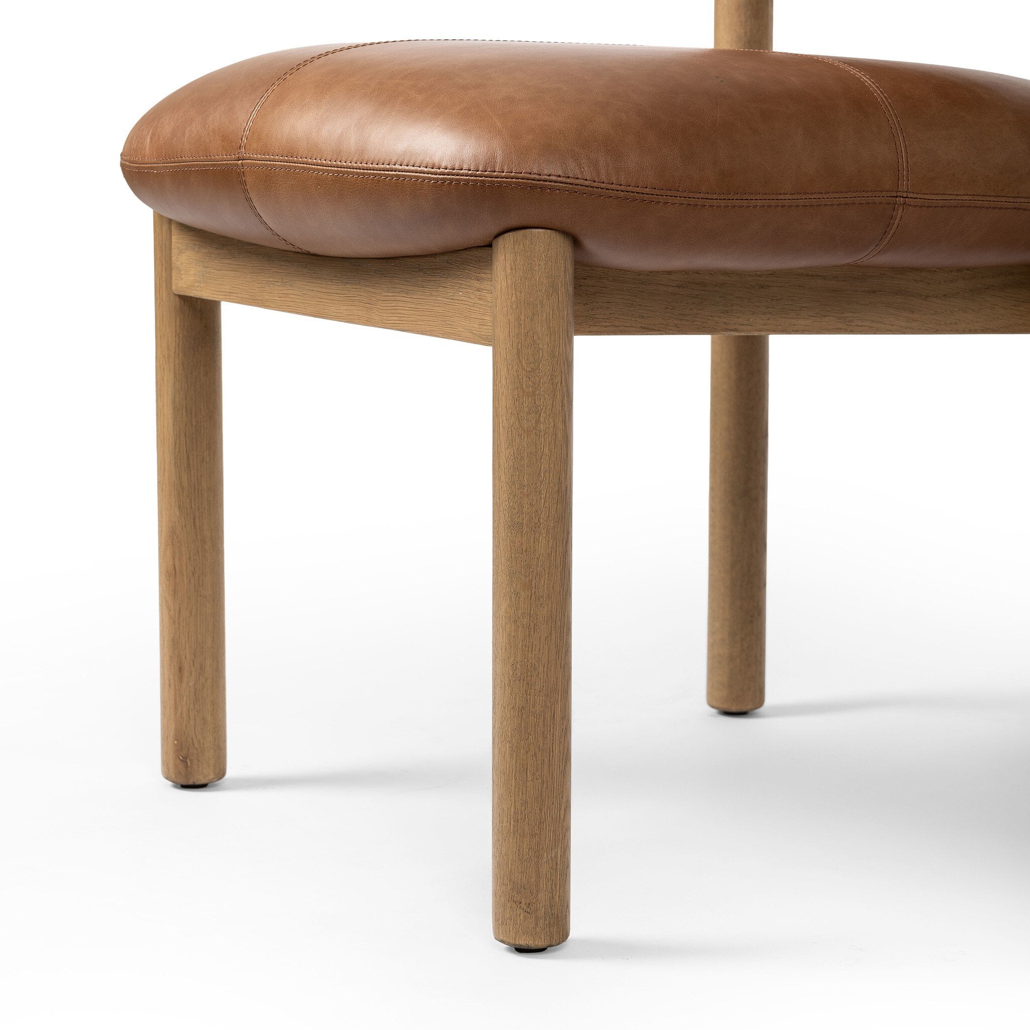 Close up of a brown leather dining chair with wooden frame on a white background.