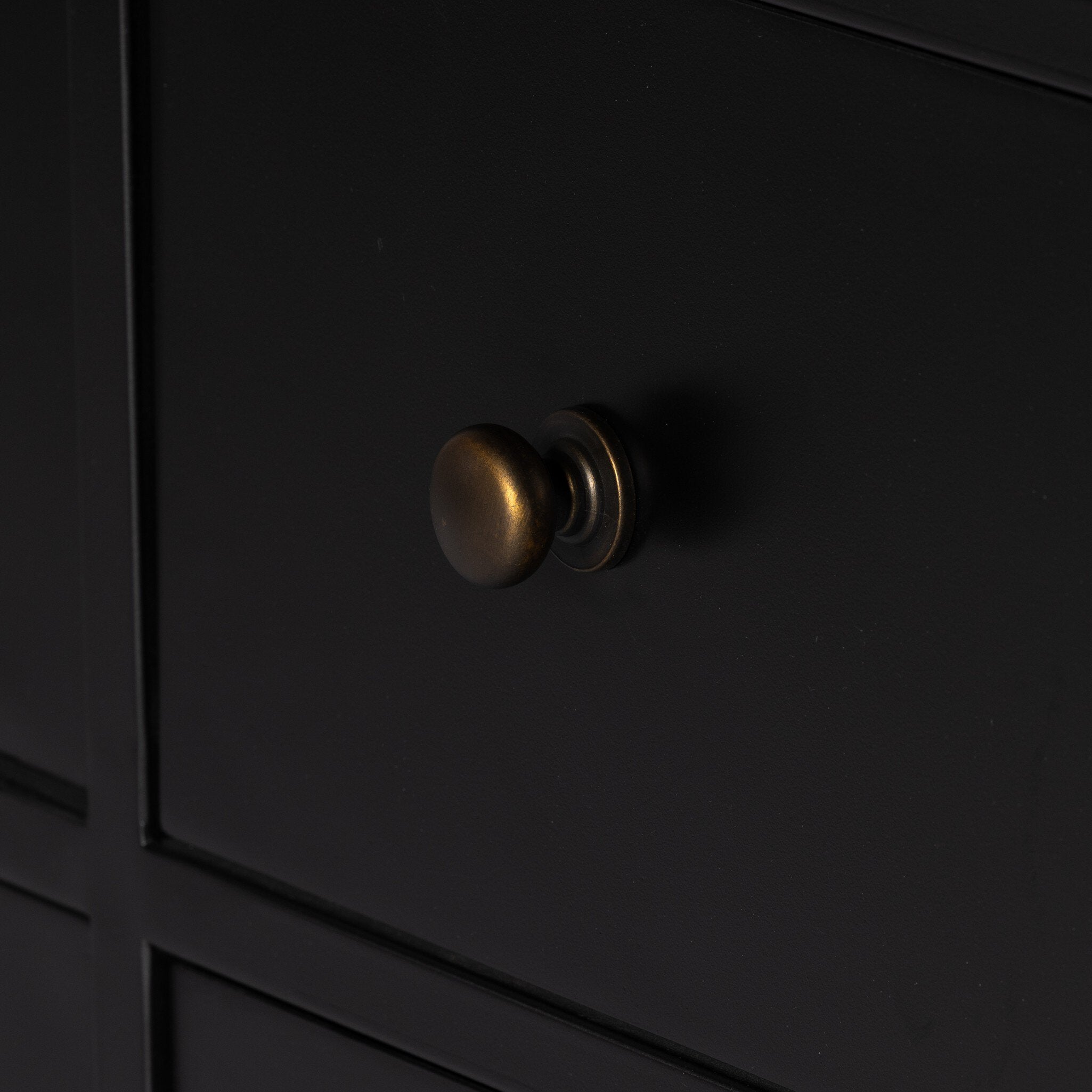 Close up of a black dresser with twelve drawers and bronze knobs on a white background.