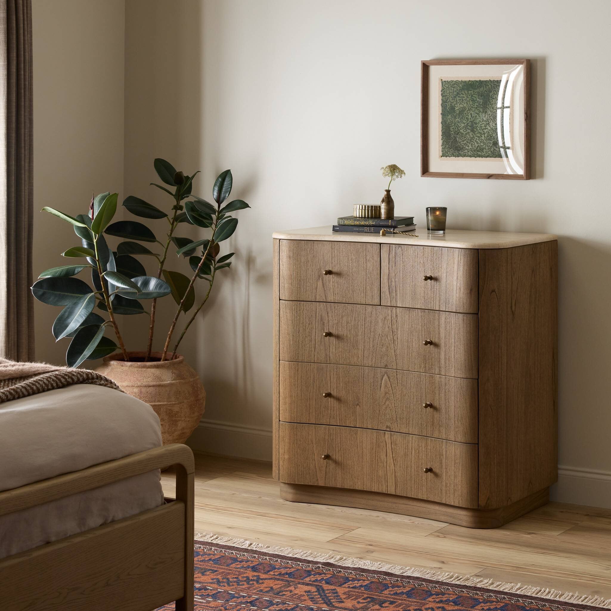 Wooden dresser in a bedroom with a plant and framed picture on top. | Wildwood Home Co.