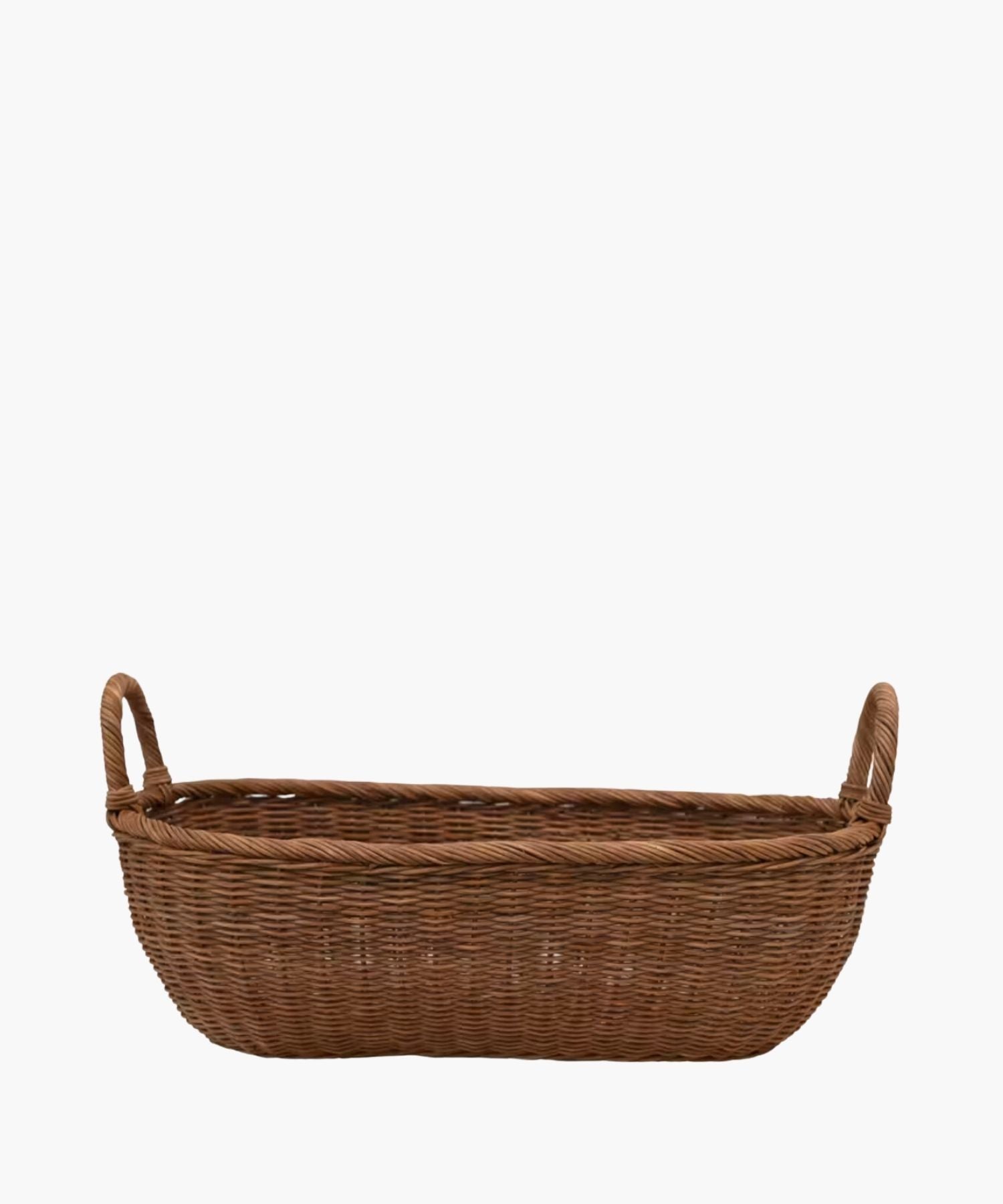 A handwoven wicker basket with two looped handles on either side featuring an organic oval shape and a natural brown finish. The basket has a natural, rustic appearance. | Wildwood Home Co.