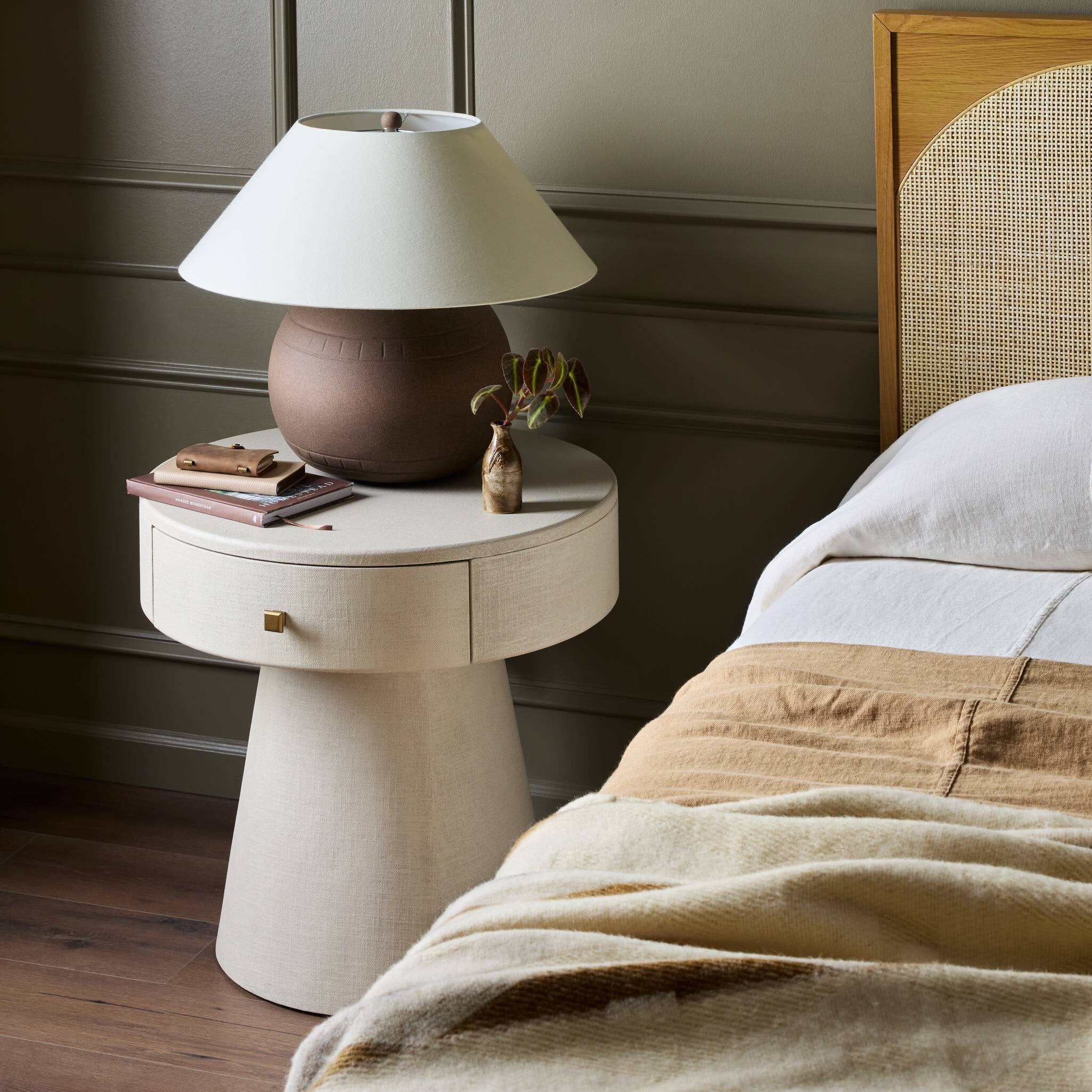 White nightstand with a lamp next to a bed with beige bedding. | Wildwood Home Co.