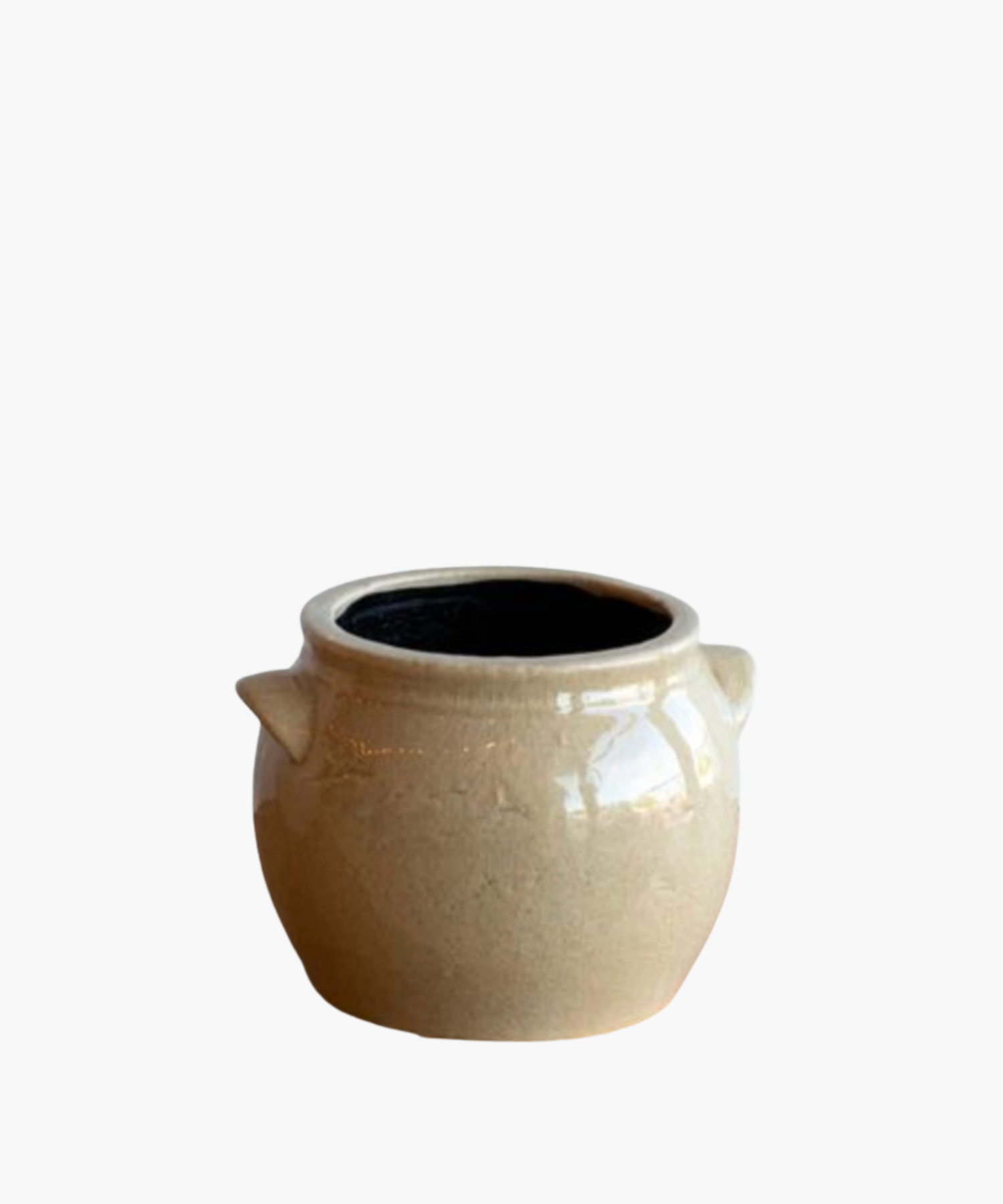 A beige ceramic pot with a glossy finish, featuring two small side handles and a black interior. The pot has a smooth, rounded shape and exudes a rustic charm. | Wildwood Home Co.
