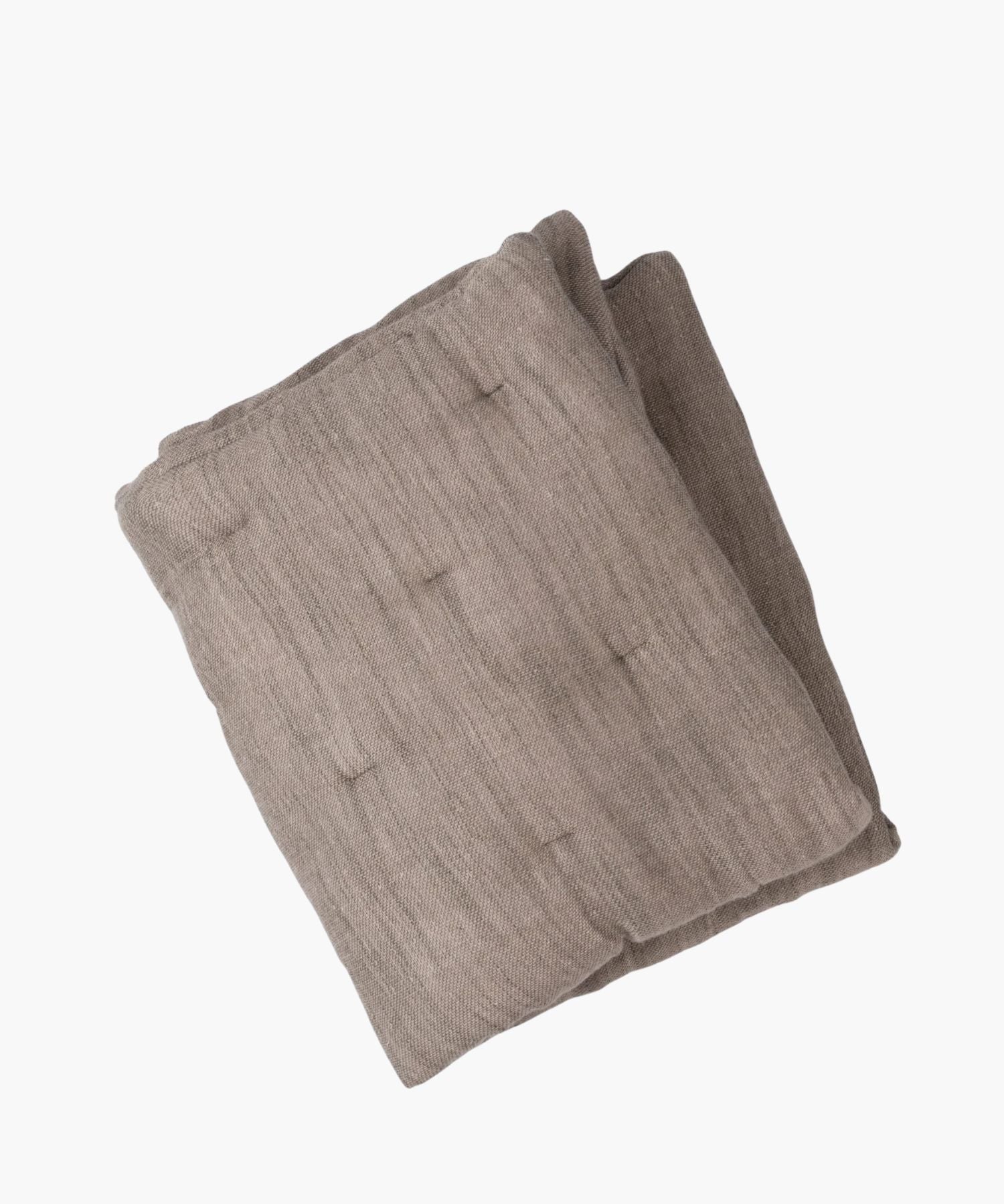 Folded neutral brown quilt on a white background showing its fabric texture.
