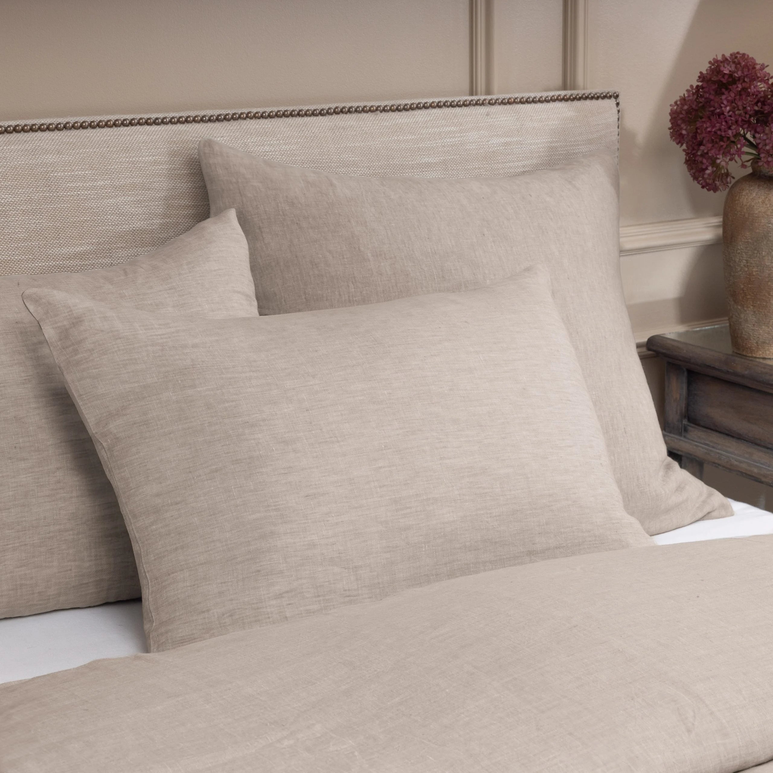 Beige textured pillows on a bed with a neutral headboard and side table. | Wildwood Home Co.