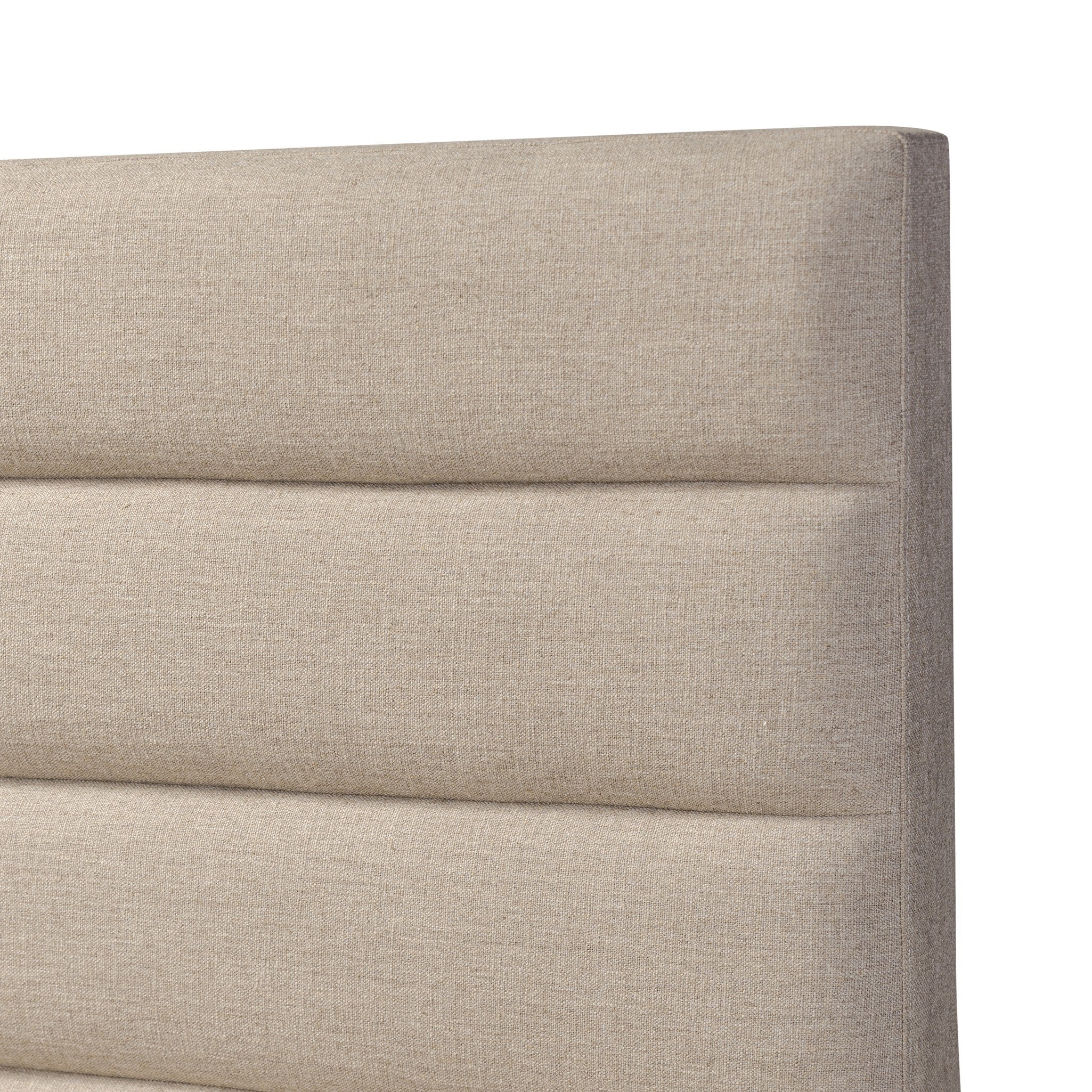 Close up of a taupe upholstered bed with horizontal channeling on the headboard and white bedding on a white background.