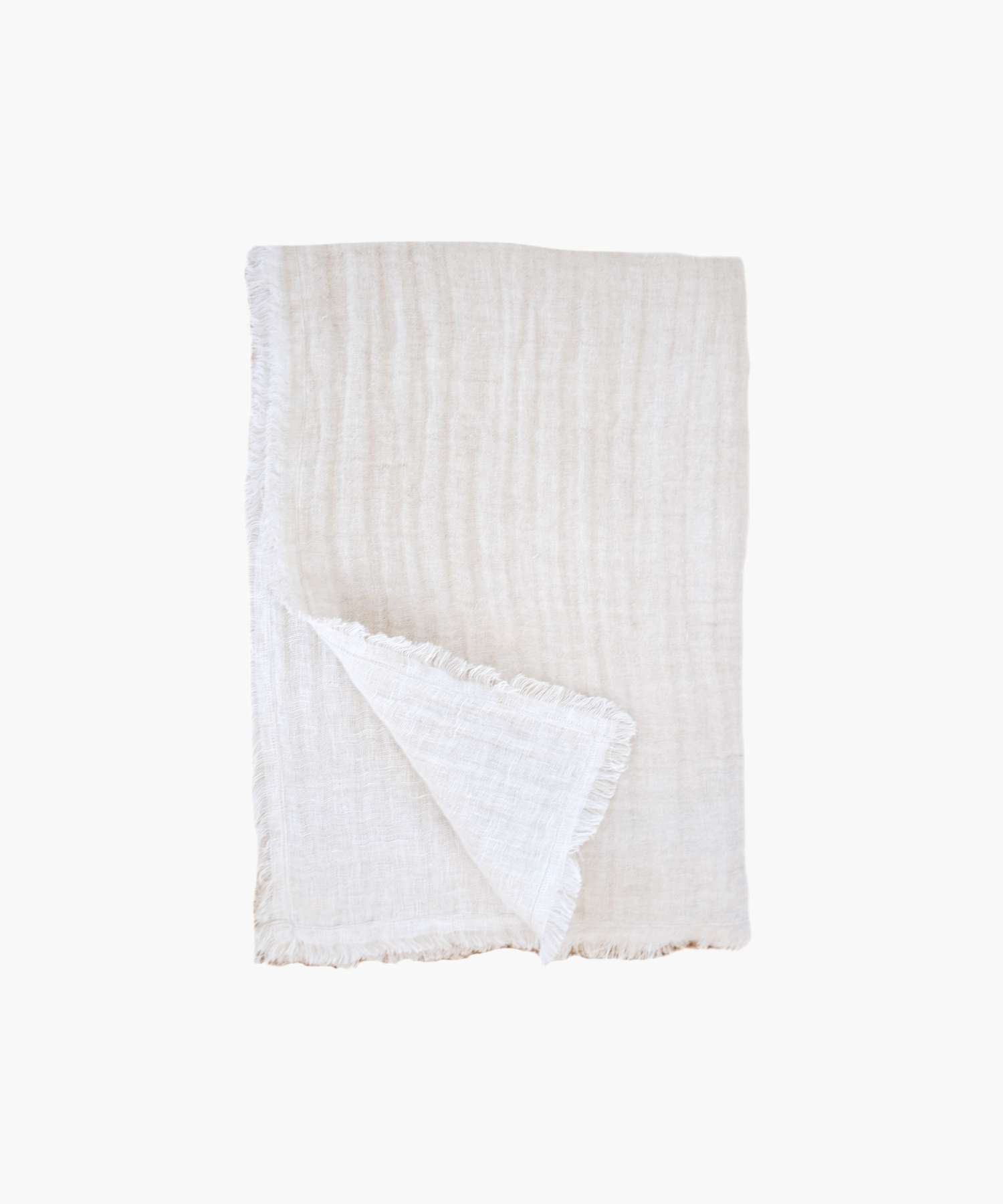 A soft, beige linen throw blanket is neatly folded against a plain background, showcasing a delicate fringe along the edges, conveying a cozy and elegant feel. | Wildwood Home Co.