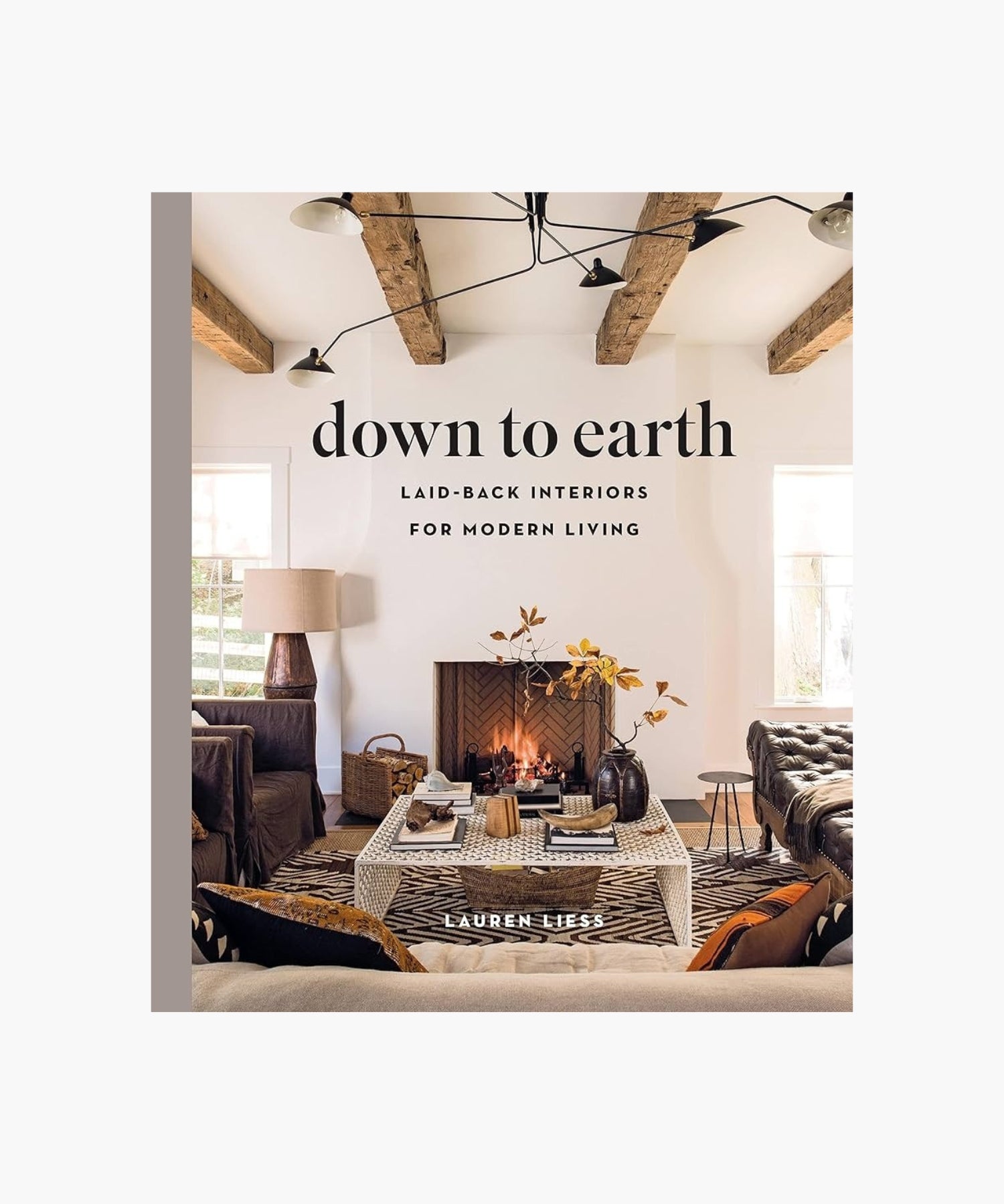 The cover of the book "Down to Earth" by Lauren Liess features a living room with a cozy fireplace, rustic wooden beams, a patterned rug, and modern furniture. The atmosphere is warm and inviting. | Wildwood Home Co.