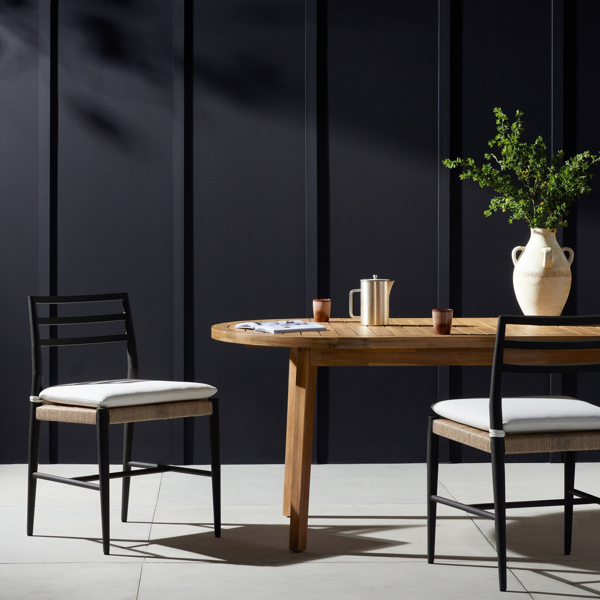 Outdoor dining table with chairs against a dark paneled wall. | Wildwood Home Co.