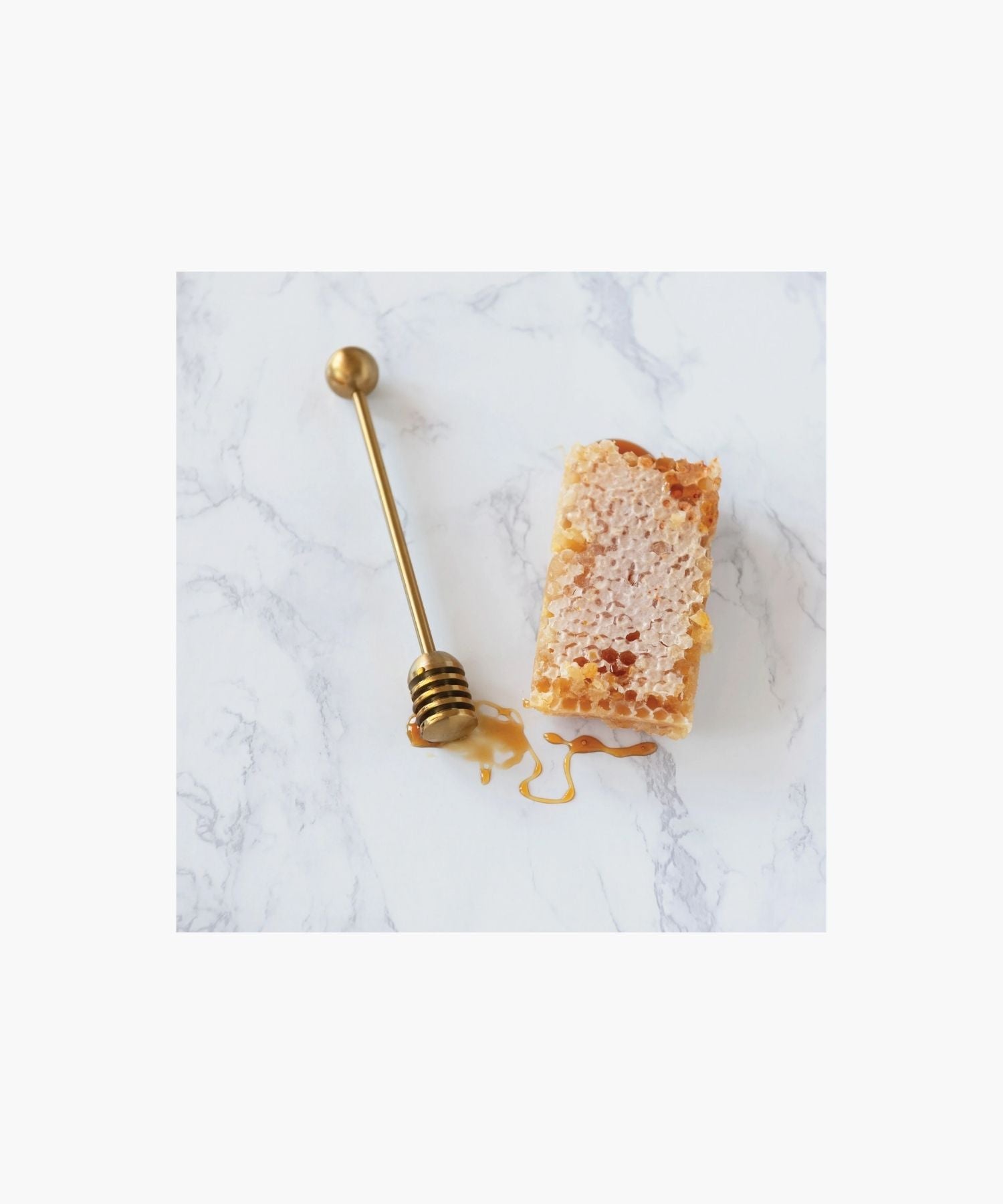 Gold honey dipper with a round handle and grooved end for collecting honey styled with honey comb on a marble surface. Simple and elegant kitchen tool. | Wildwood Home Co.