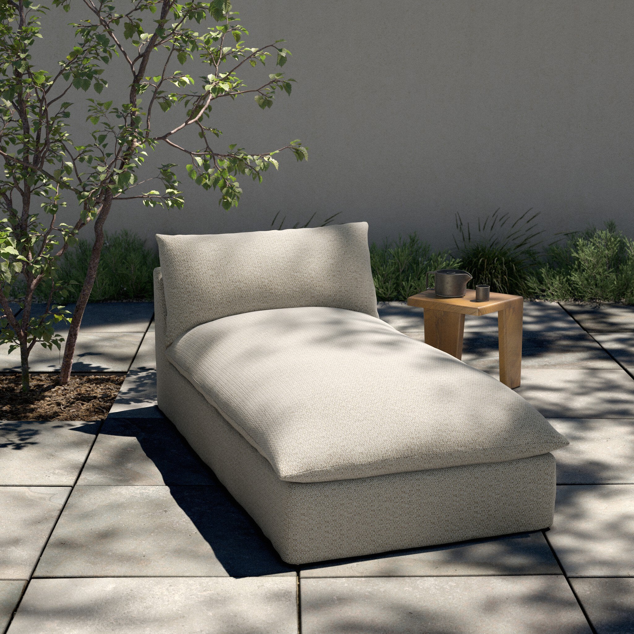Beige outdoor chaise lounge on a patio with plants and a table in the background.
