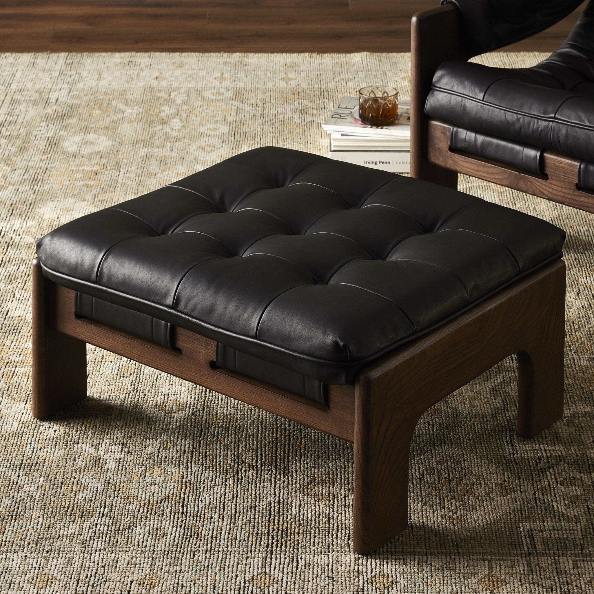 Black leather ottoman with wooden frame on a textured rug. | Wildwood Home Co.