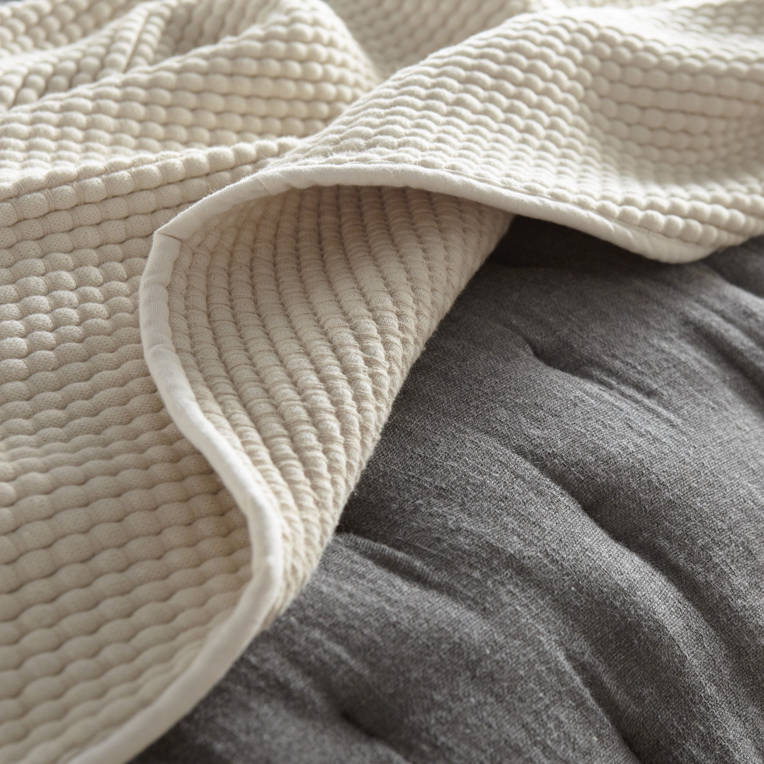 Ivory coverlet styled in natural light on a dark neutral background, showing fabric texture, material color, and relaxed drape. | Wildwood Home Co.
