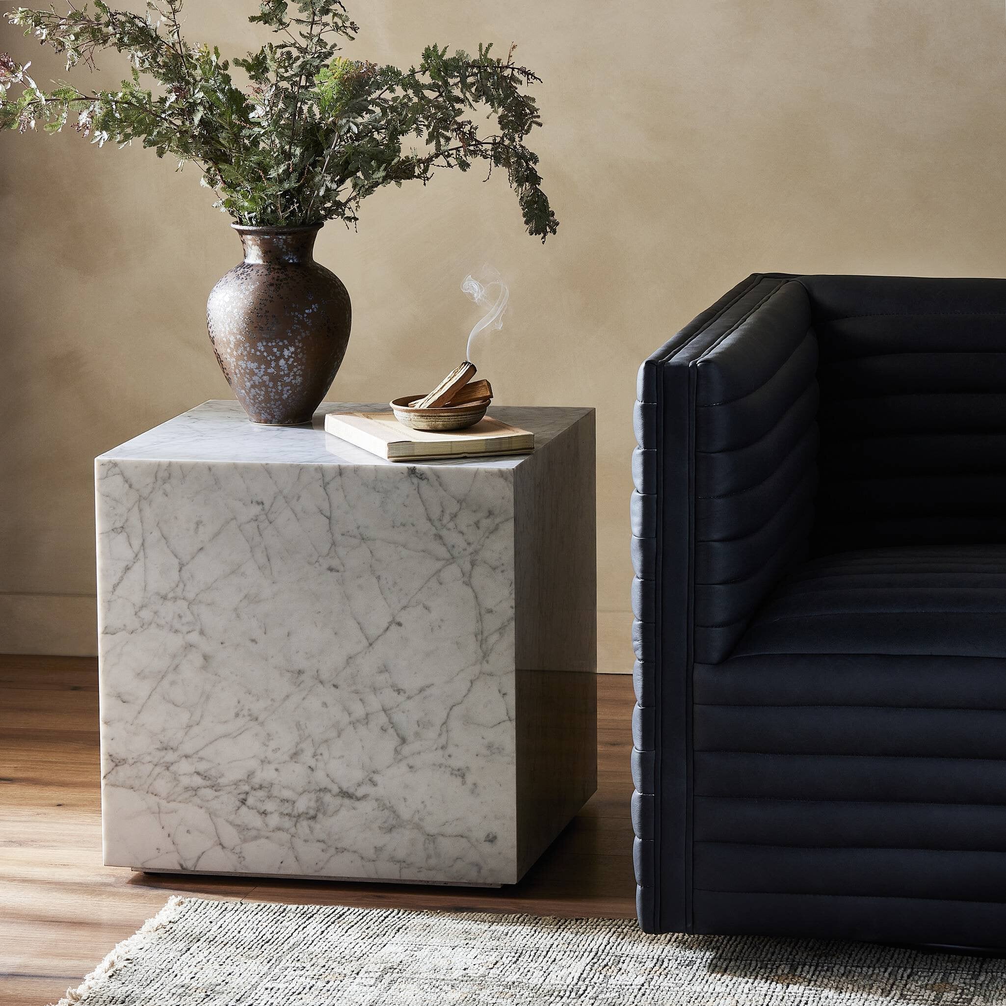 Marble side table with decorative items next to a black sofa. | Wildwood Home Co.