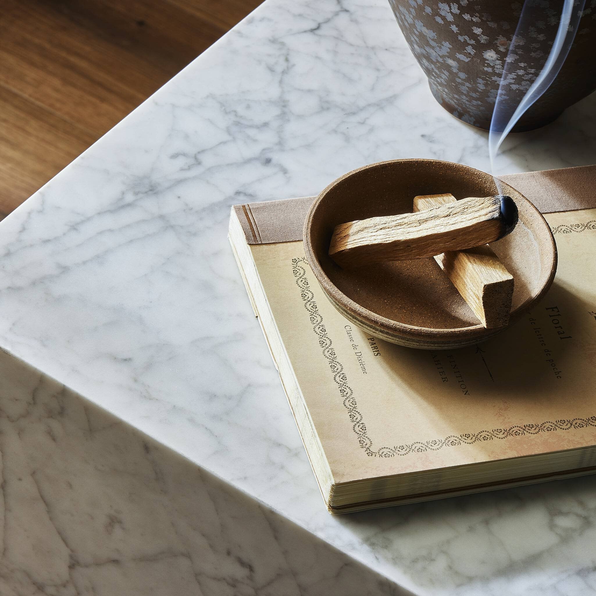 Wooden bowl with incense sticks on an open book on a marble end table.