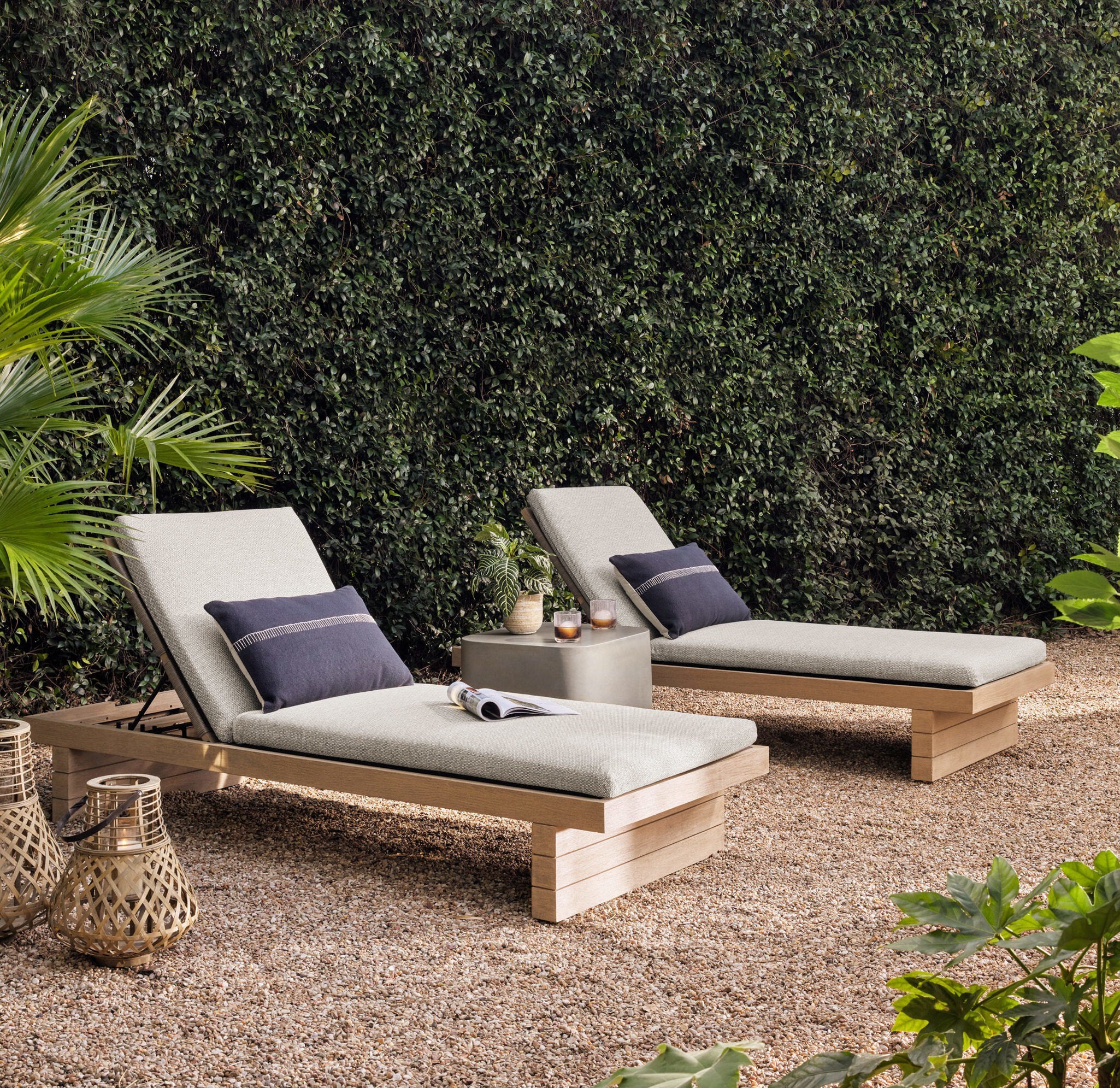 Two outdoor lounge chairs with cushions on a gravel surface with greenery in the background. | Wildwood Home Co.
