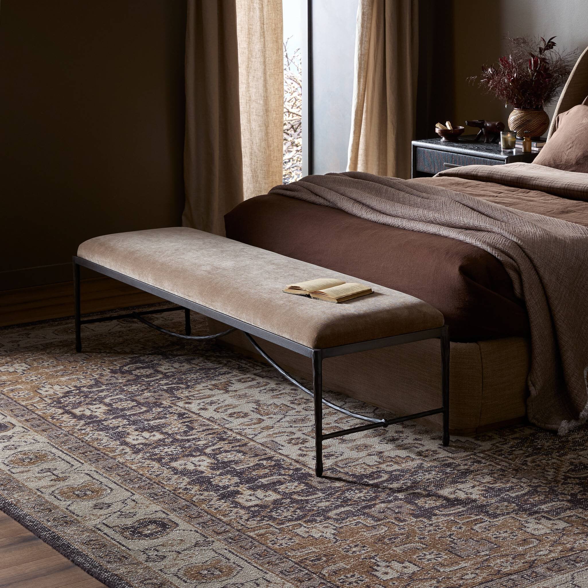 Beige bench with a book on a patterned rug in a bedroom setting. | Wildwood Home Co.