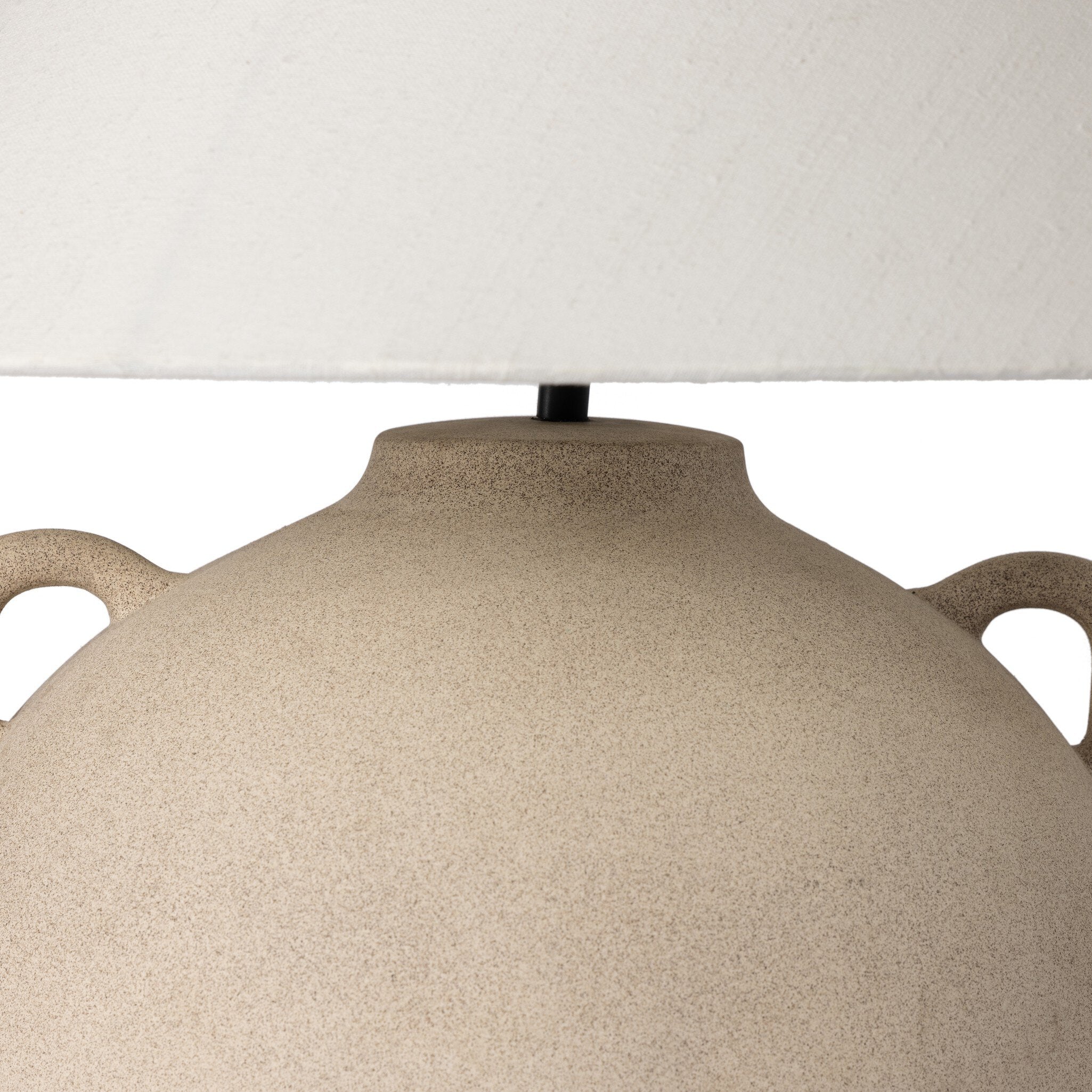 Close up of a beige ceramic table lamp with an ivory lampshade on a white background.
