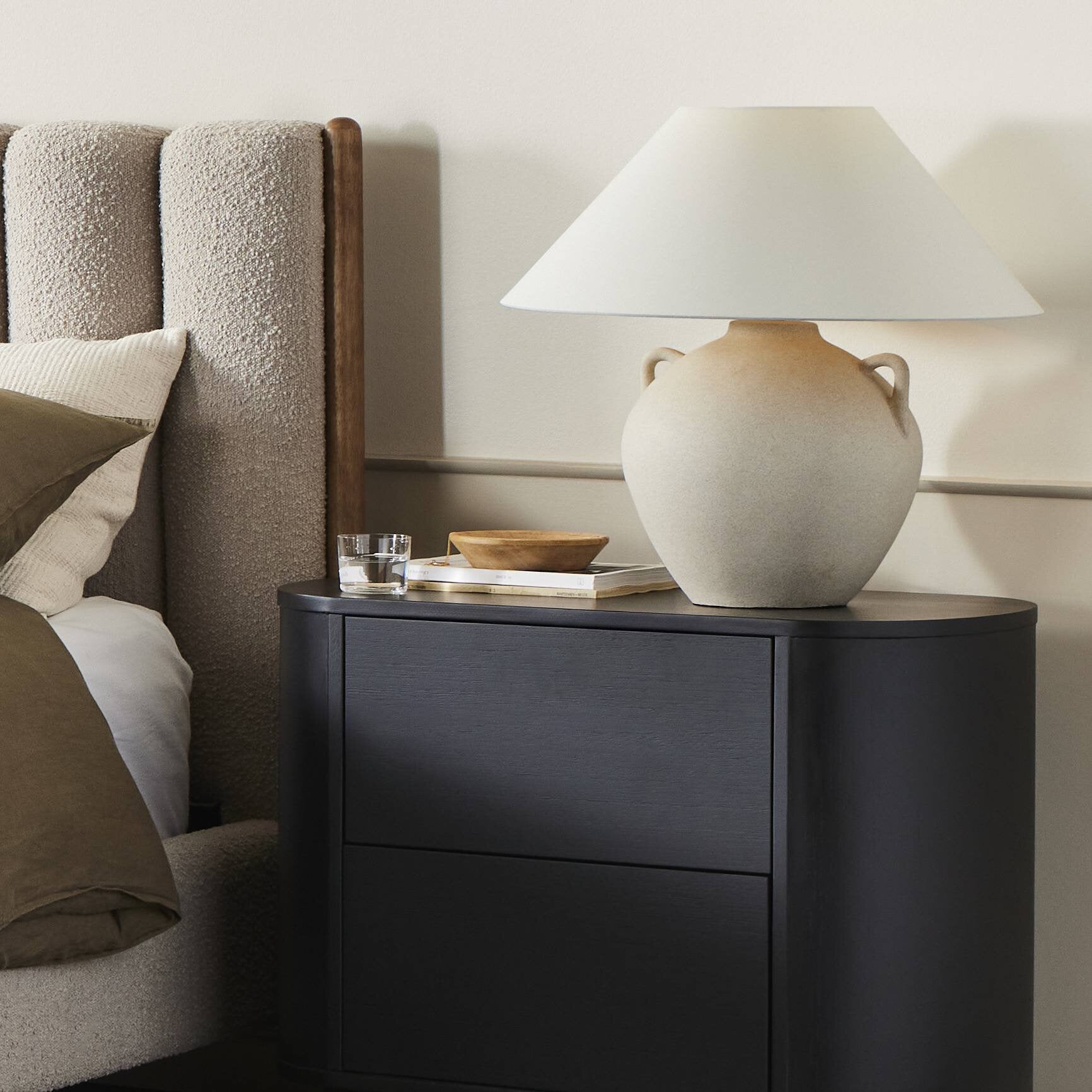 Black nightstand with a lamp and decorative items next to a bed. | Wildwood Home Co.