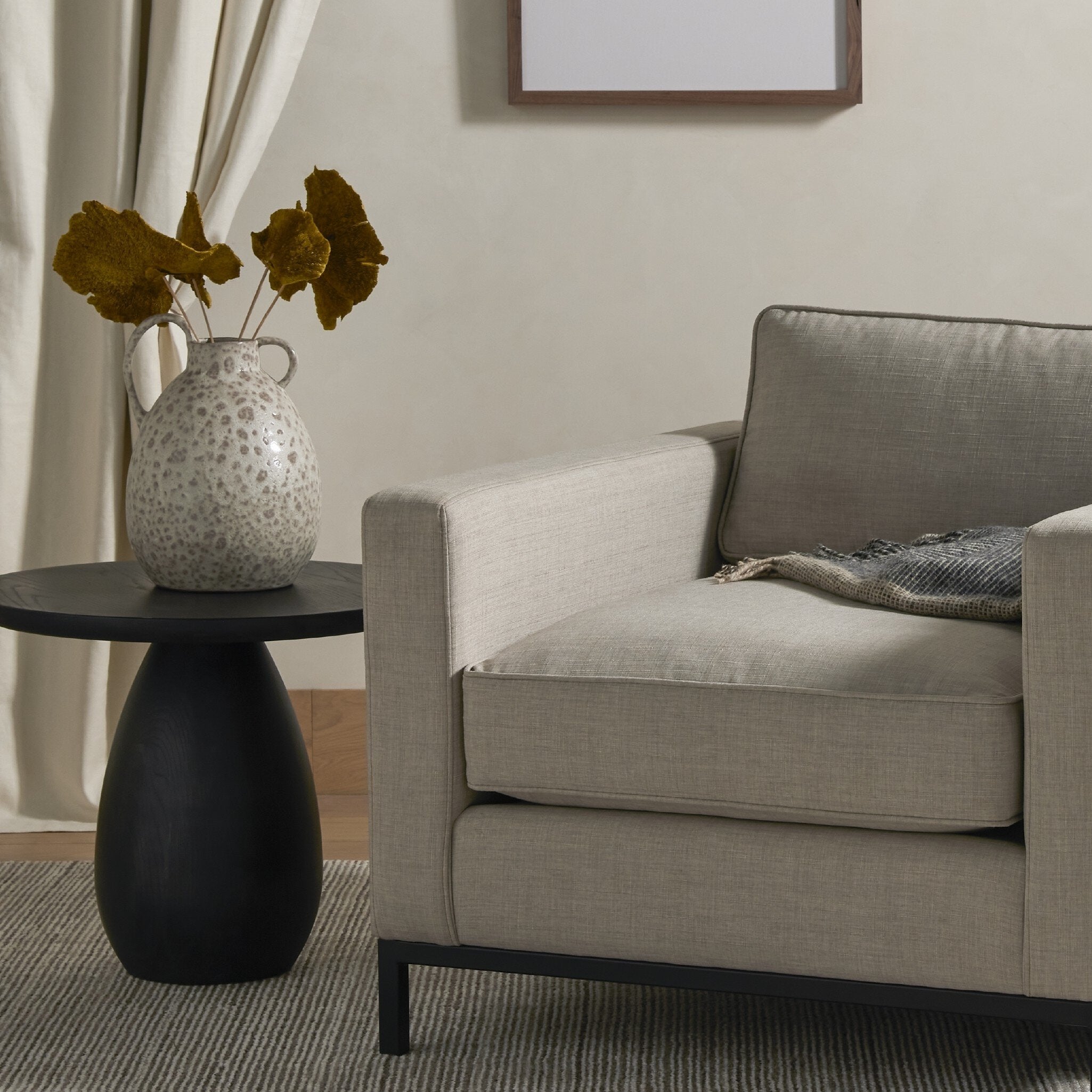 Gray chair in a living room with a black side table and decorative vase.