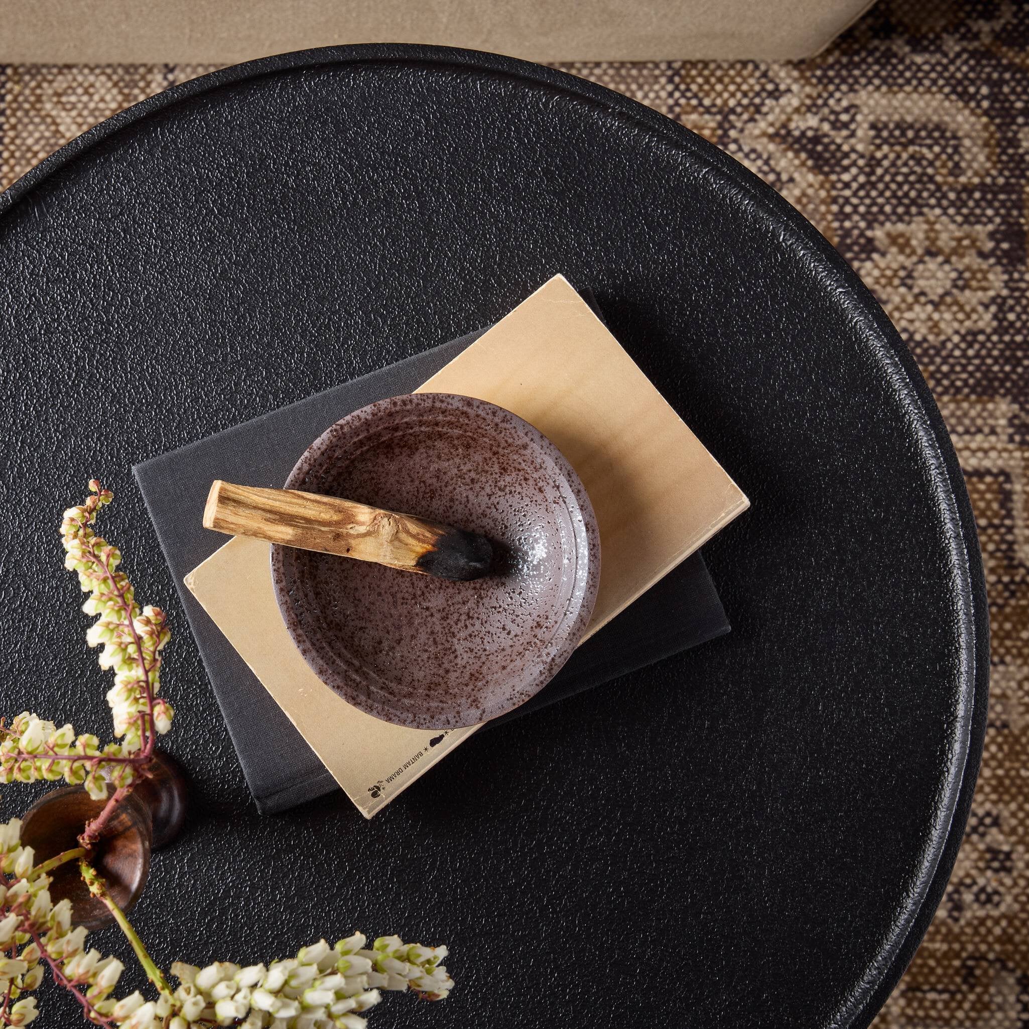 Brown ceramic bowl with wooden spoon styled on a textured black end table.
