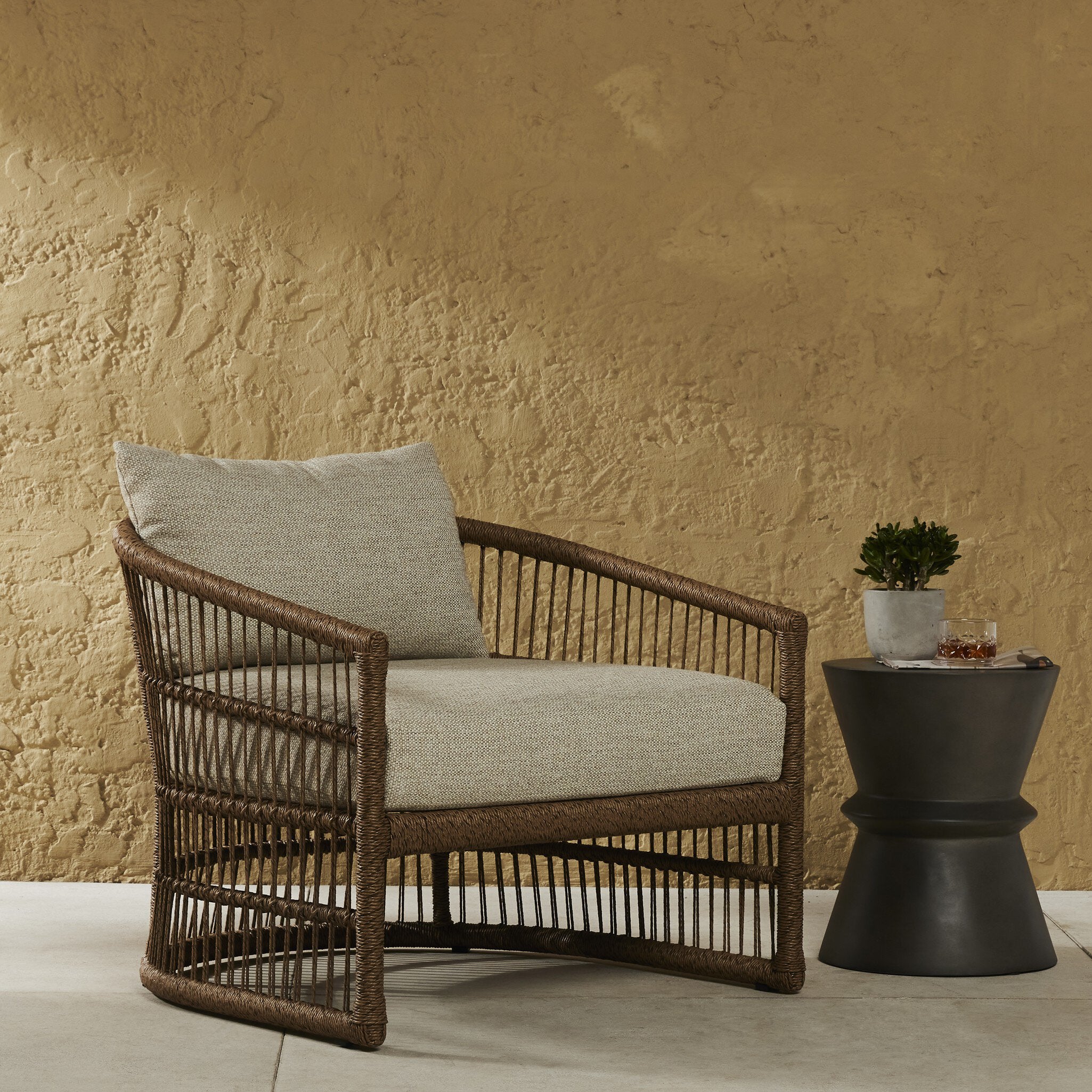 Wicker chair with cushions against a textured beige wall. | Wildwood Home Co.