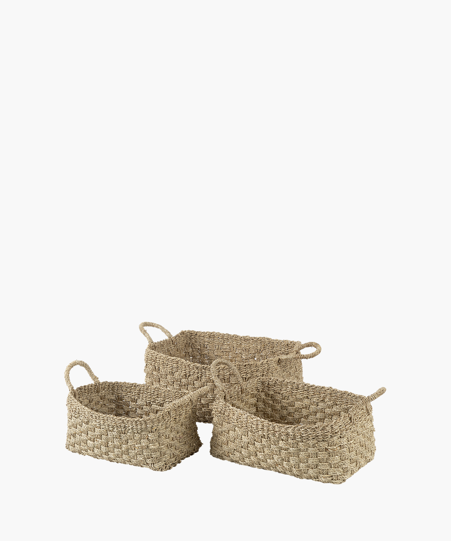 Three rectangular seagrass woven baskets in various sizes with two looped handles, made of natural fibers in a textured, checkerboard pattern. The tone is earthy and rustic.