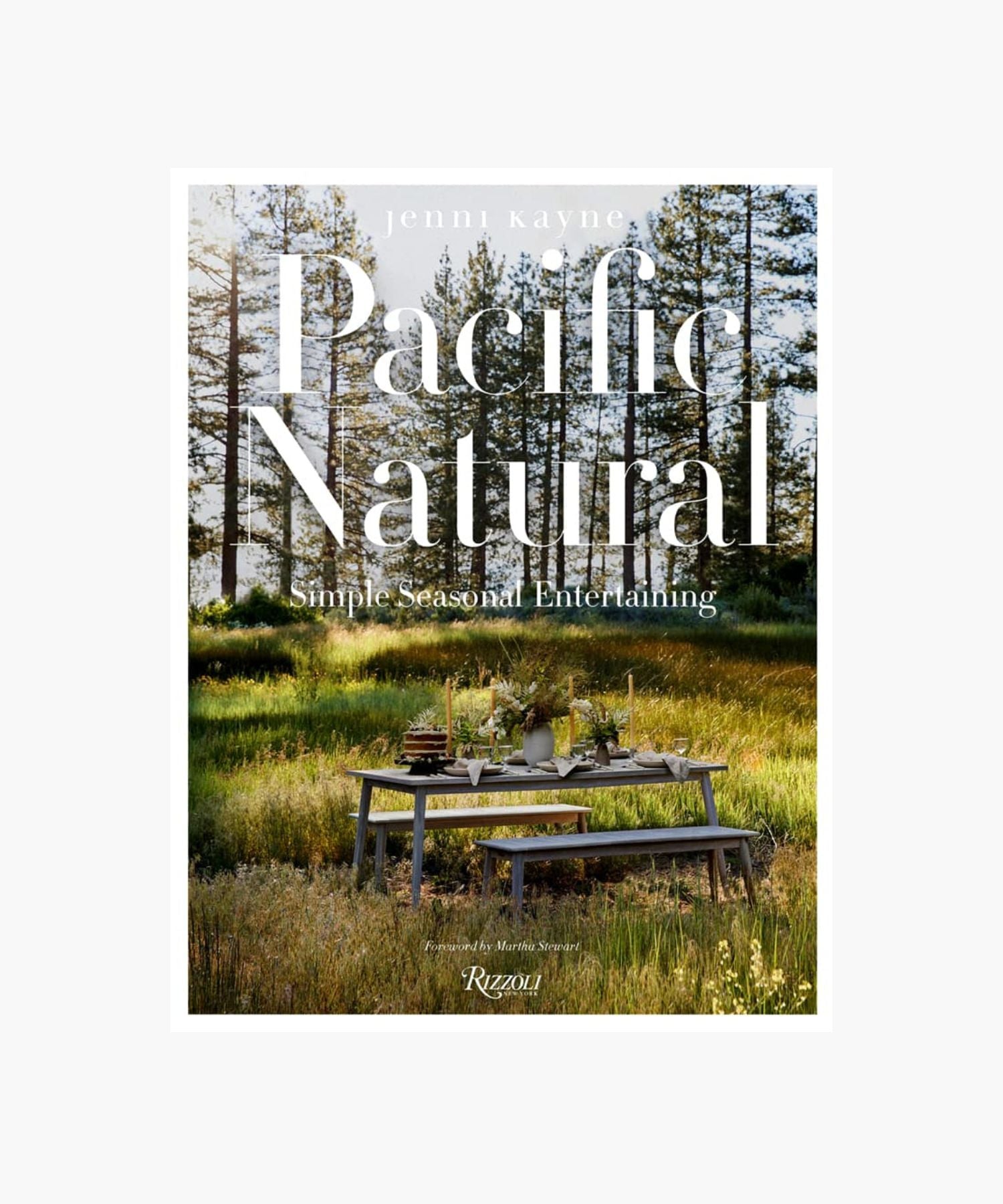 The cover of the book "Pacific Natural" by Jenni Kayne featuring a serene outdoor picnic scene with a rustic table set in a sunlit forest, conveying tranquility and elegance. | Wildwood Home Co.