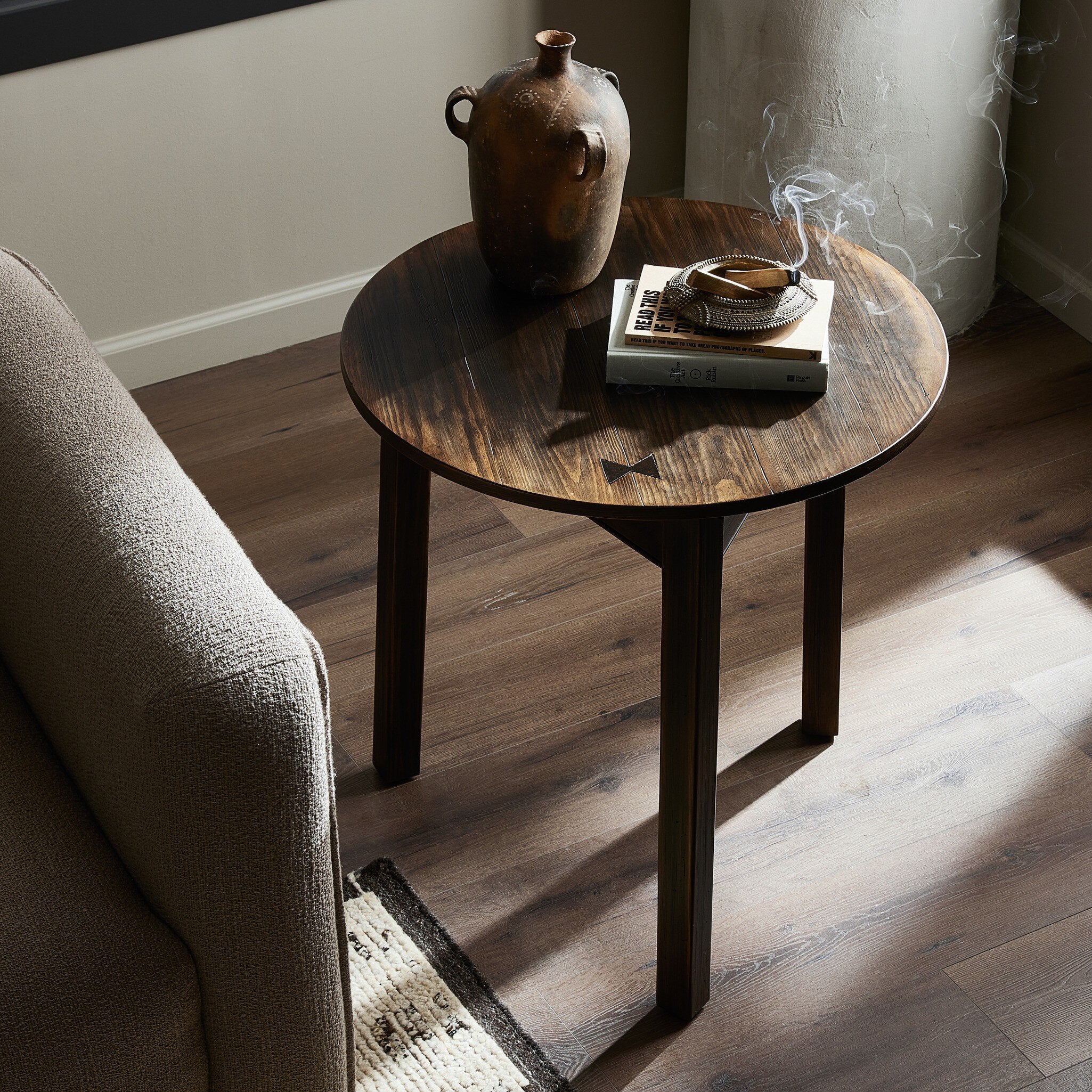 Round wooden end table with a vase and books in a room with a sofa and rug. | Wildwood Home Co.