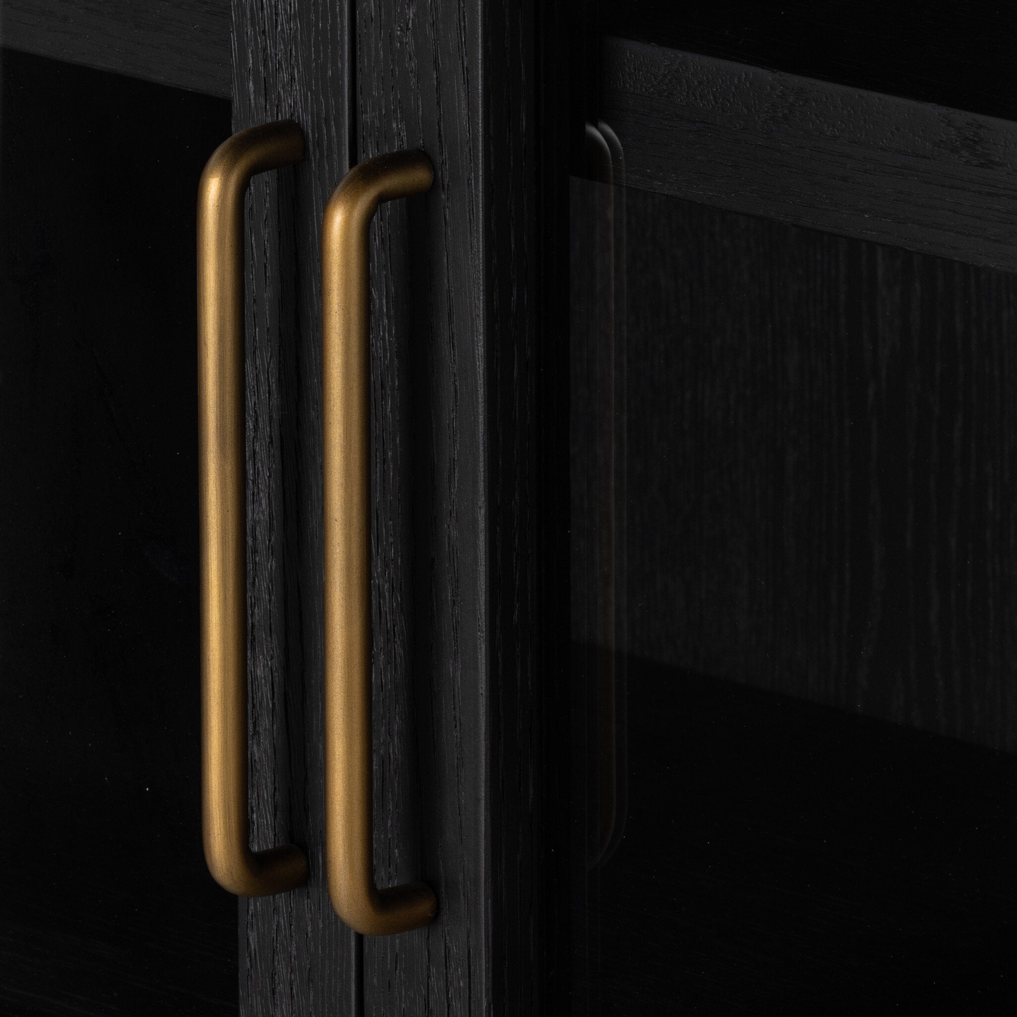Close up of the handles of a black-finished solid oak cabinet with an arched top and glass doors.
