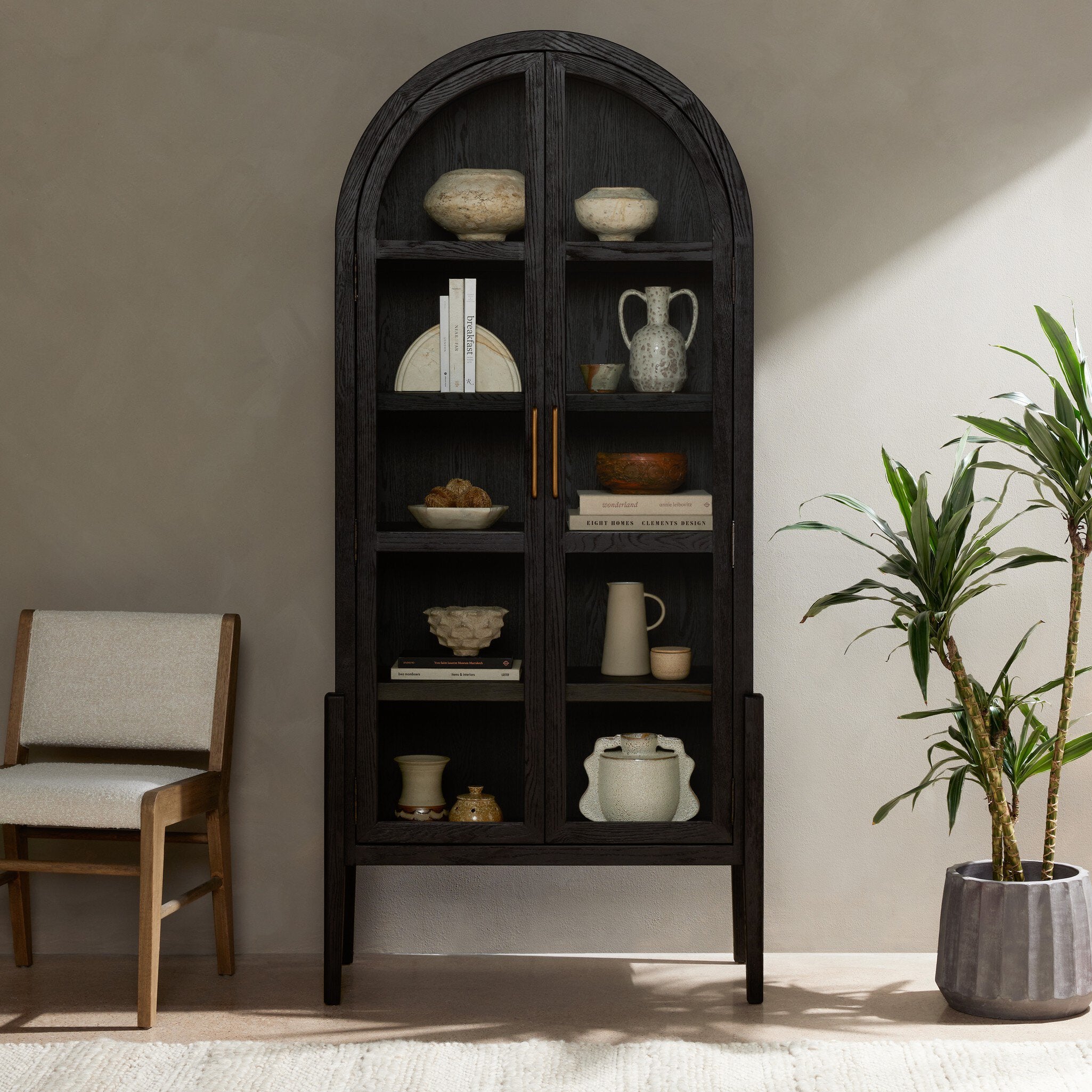 Dark wooden bookshelf with decorative items in a room with a chair and plant. | Wildwood Home Co.