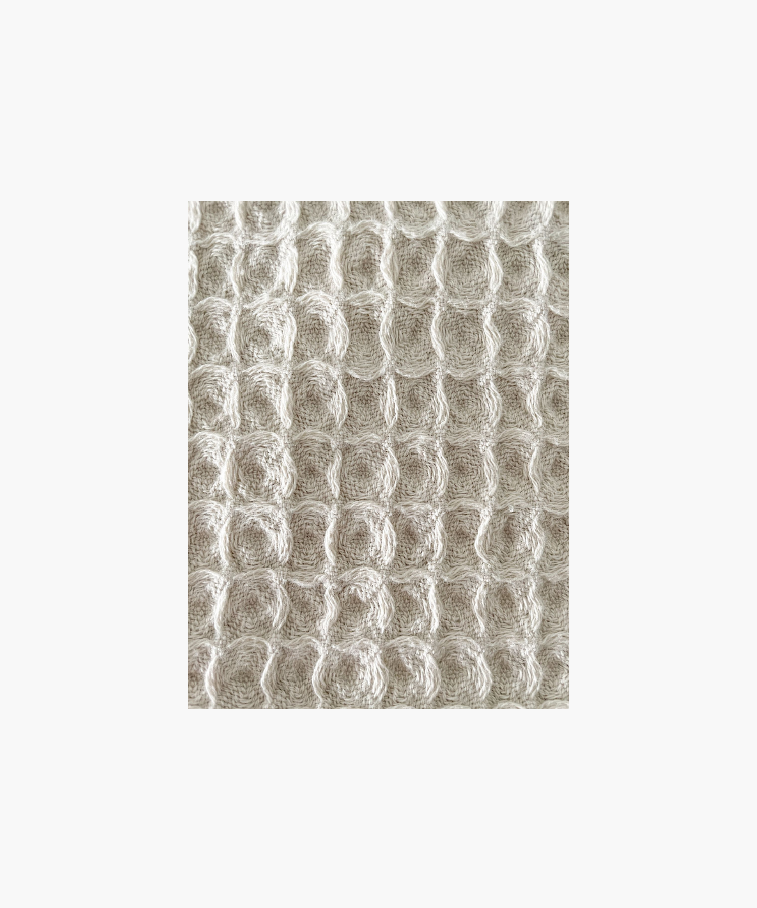 Close up of the beige waffle-textured throw blanket highlighting the texture and color. The soft material conveys a cozy, inviting feel. Suitable for any living room or bedroom.