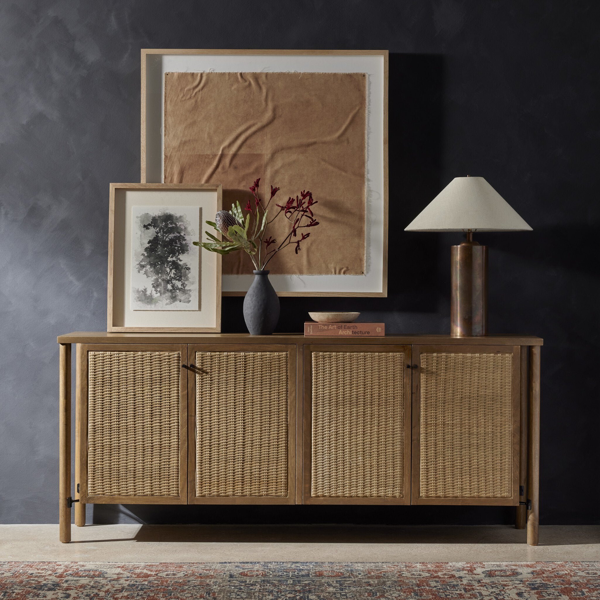 Wooden sideboard with wicker doors, framed artwork, and a lamp against a dark wall. | Wildwood Home Co.