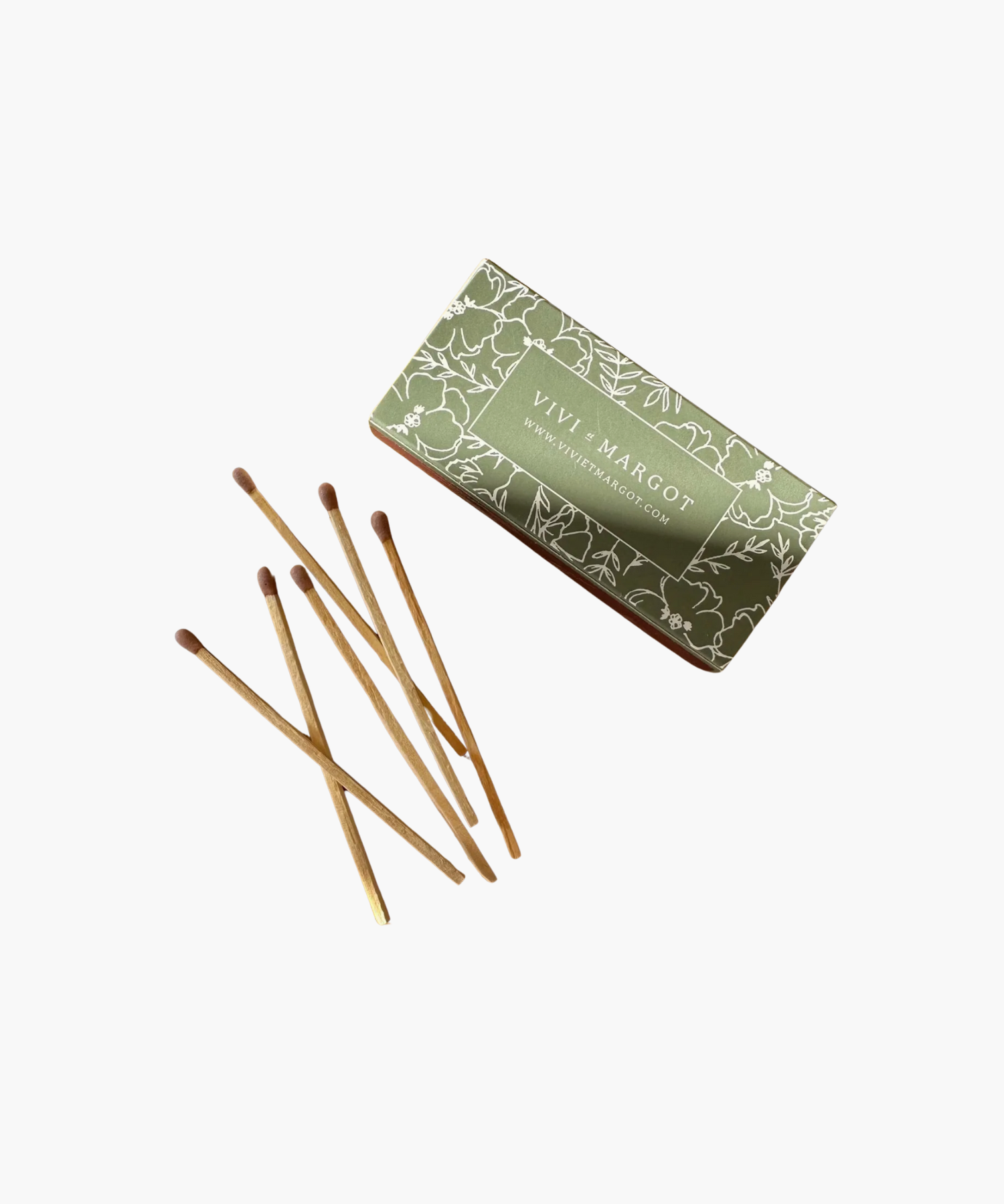 A green floral matchbox labeled "Vivi et Margot" is next to seven wooden matches with brown tips, conveying a rustic and elegant feel.