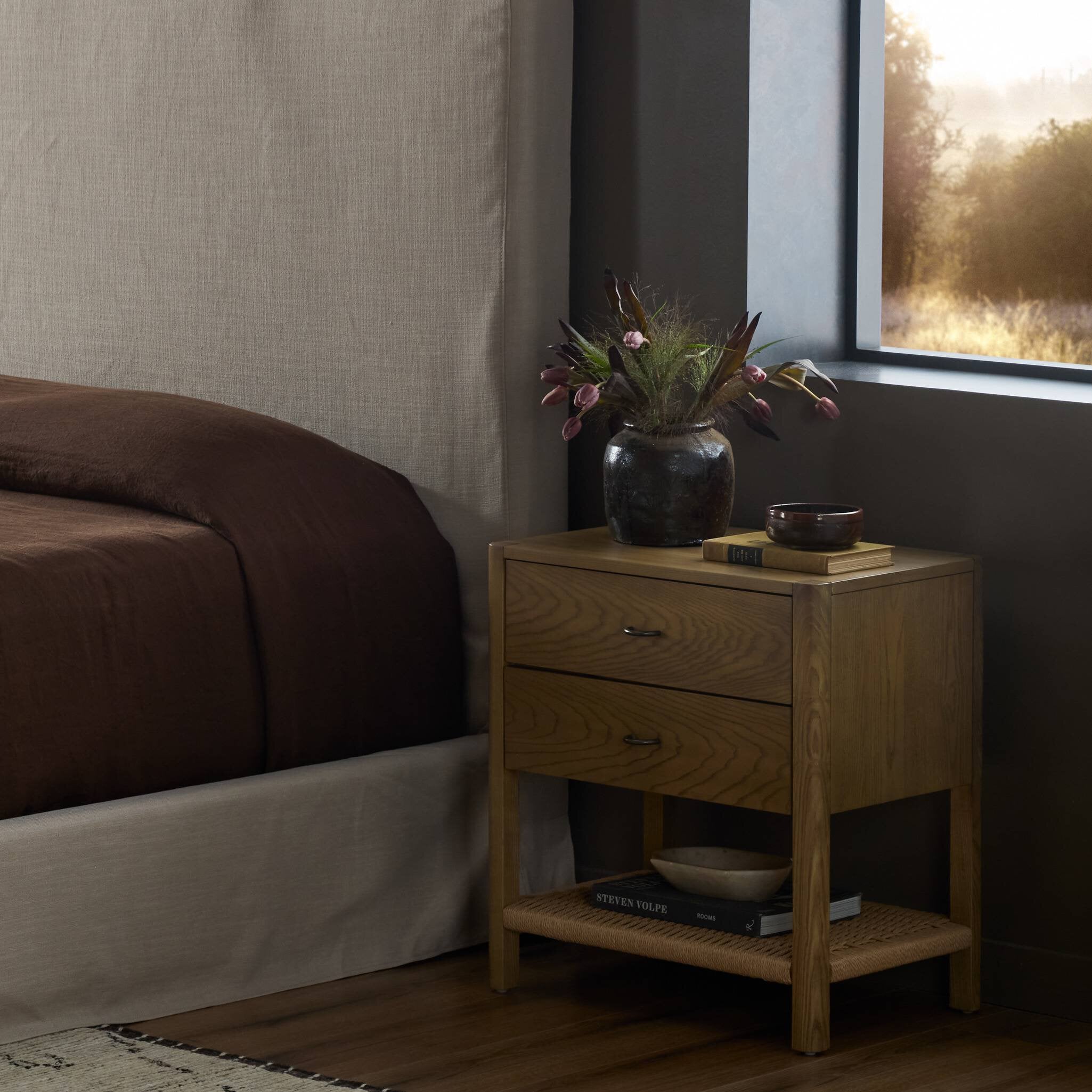 Wooden nightstand with a vase of flowers next to a bed in a bedroom. | Wildwood Home Co.