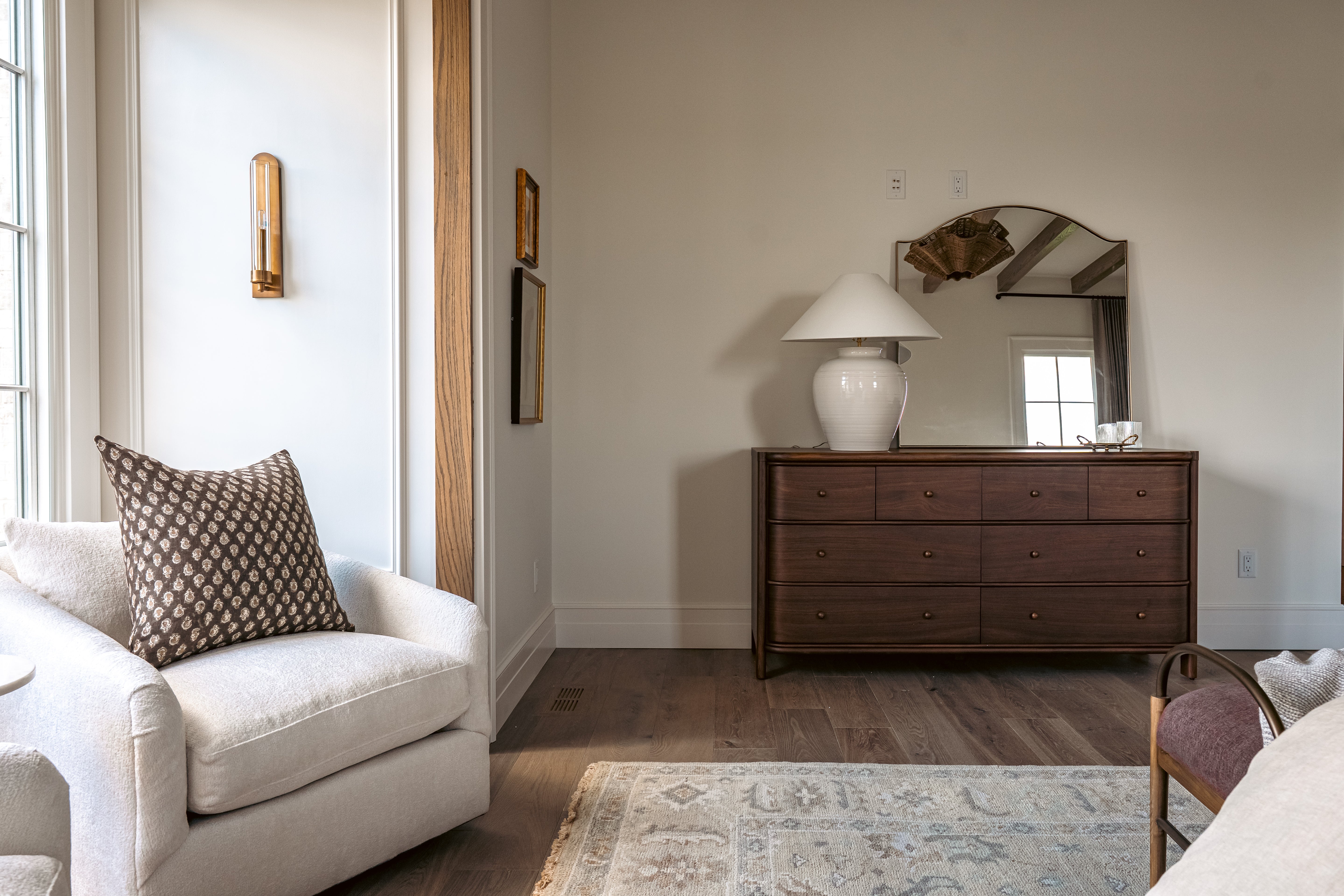Primary bedroom with a white armchair, wooden dresser, and mirror.