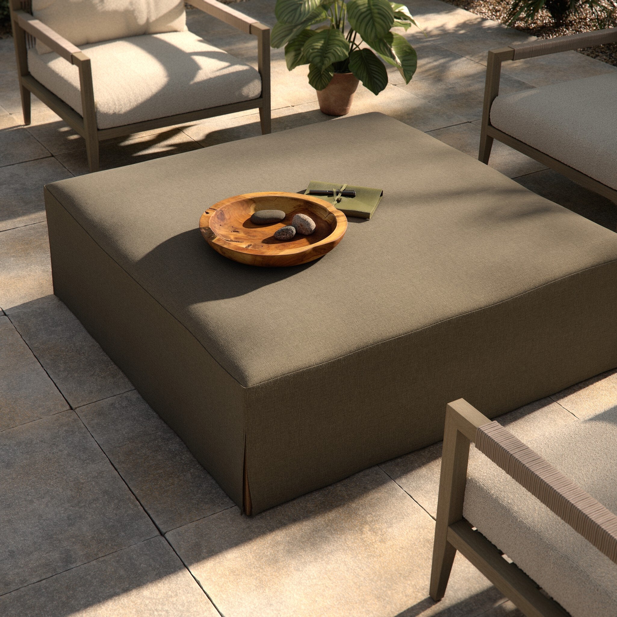 Outdoor patio setting with a square ottoman and decorative items on a stone patio. | Wildwood Home Co.