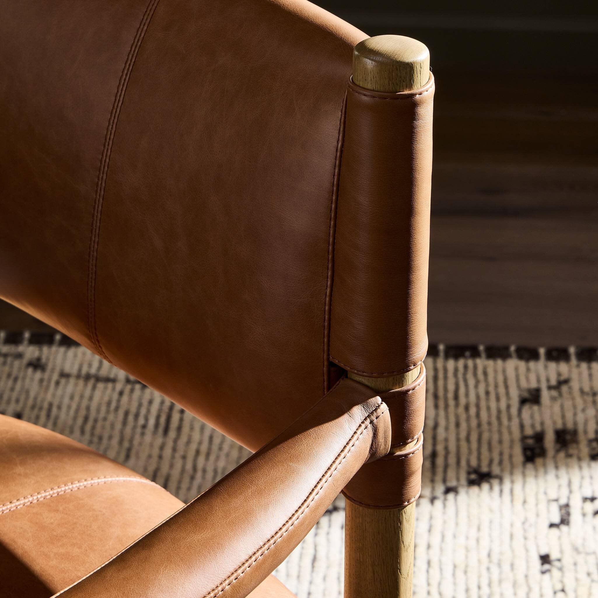 Close-up of a brown leather dining chair with wooden armrest and leg.