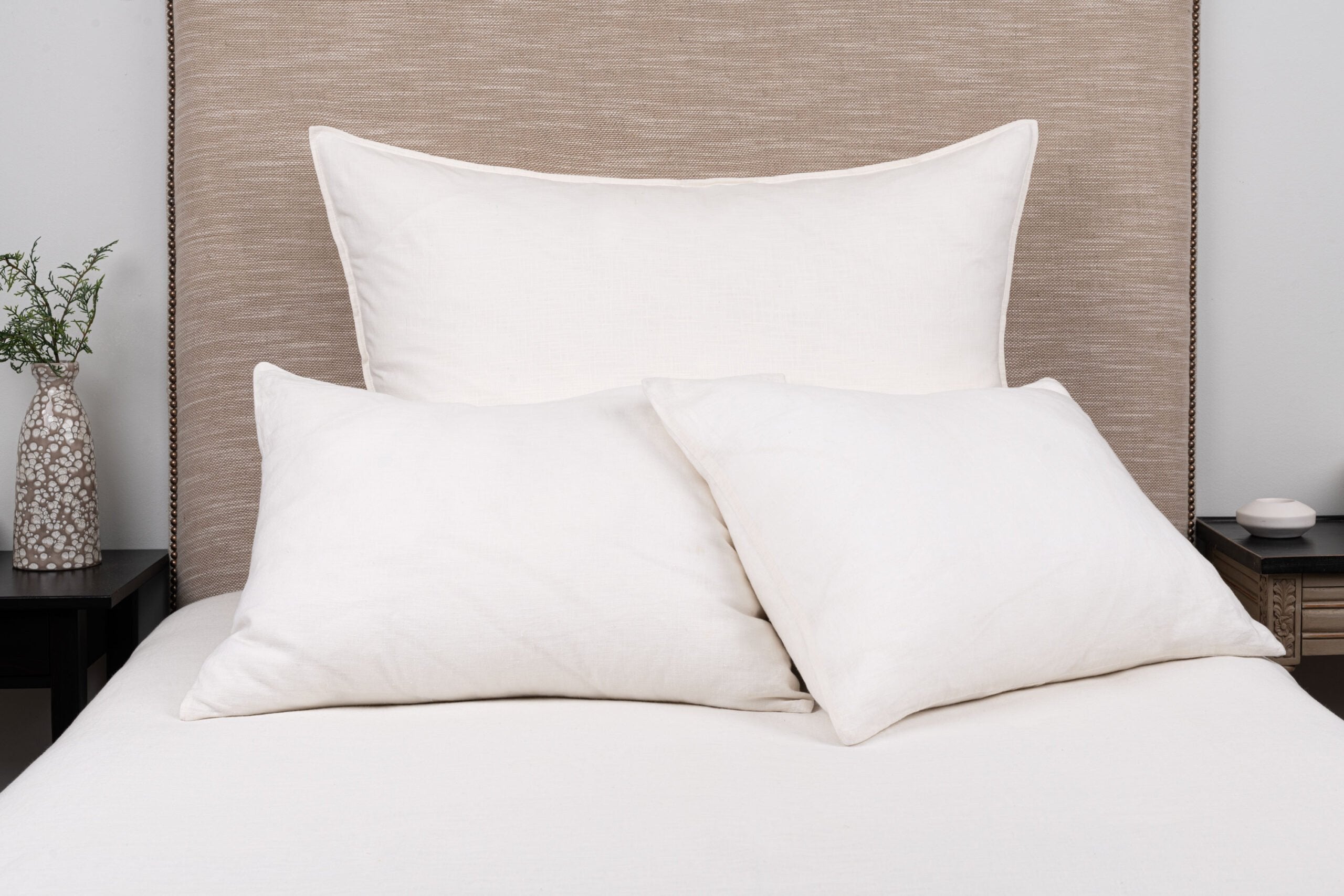 Large rectangular neutral pillow styled on a bed with smaller white pillows and white bedding with a neutral headboard and nightstands.