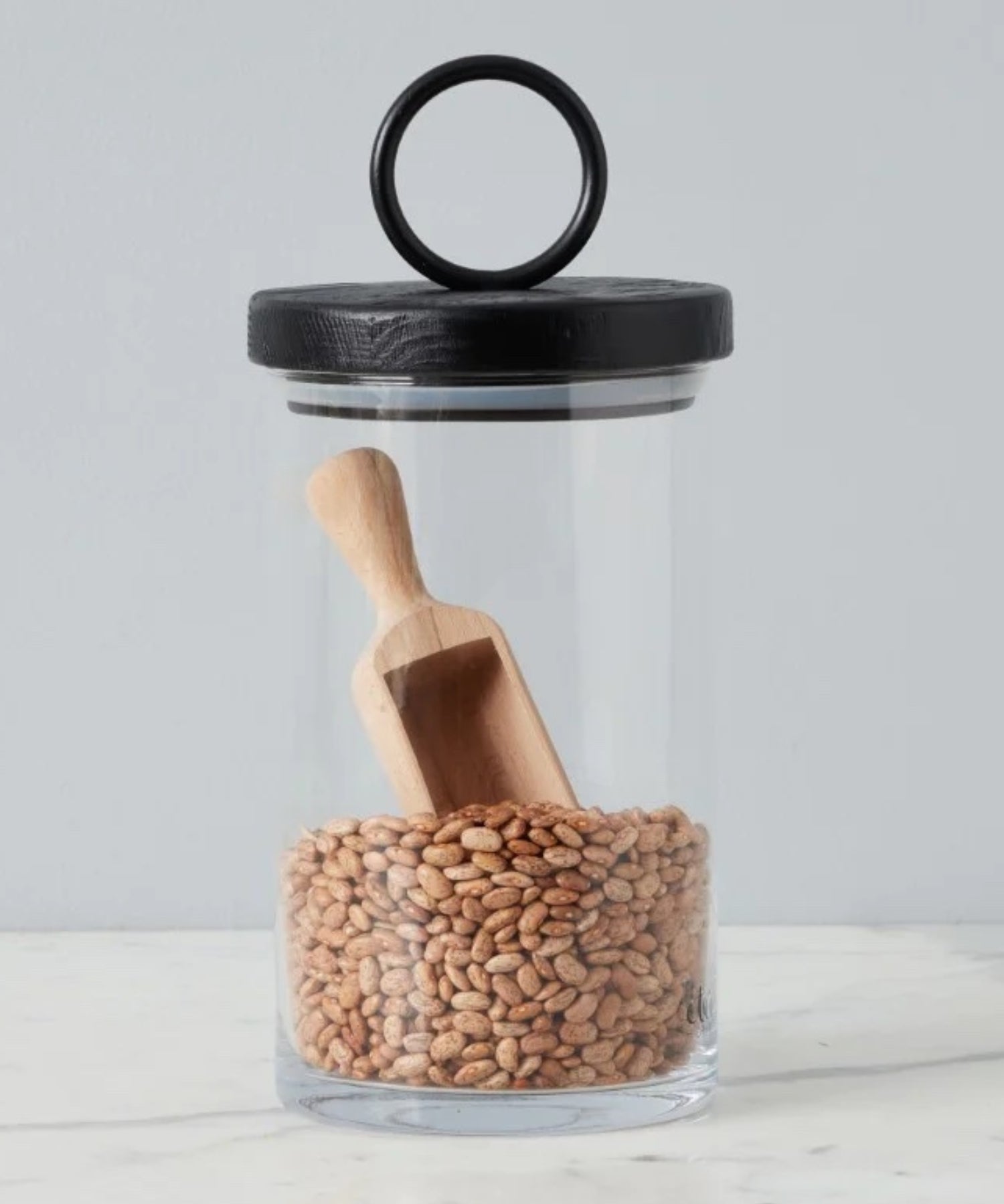 Beechwood scoop with a short handle and a broad, shallow bowl styled in a glass canister with black lid. | Wildwood Home Co.