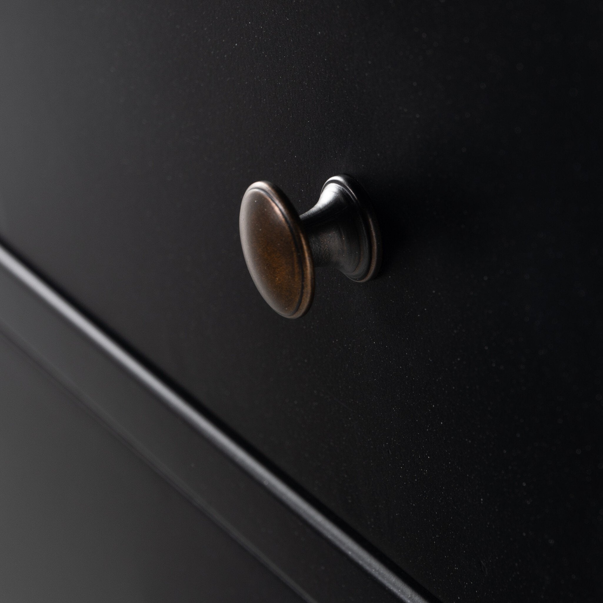A close up of a black nightstand with three drawers and metallic knobs on a white background.