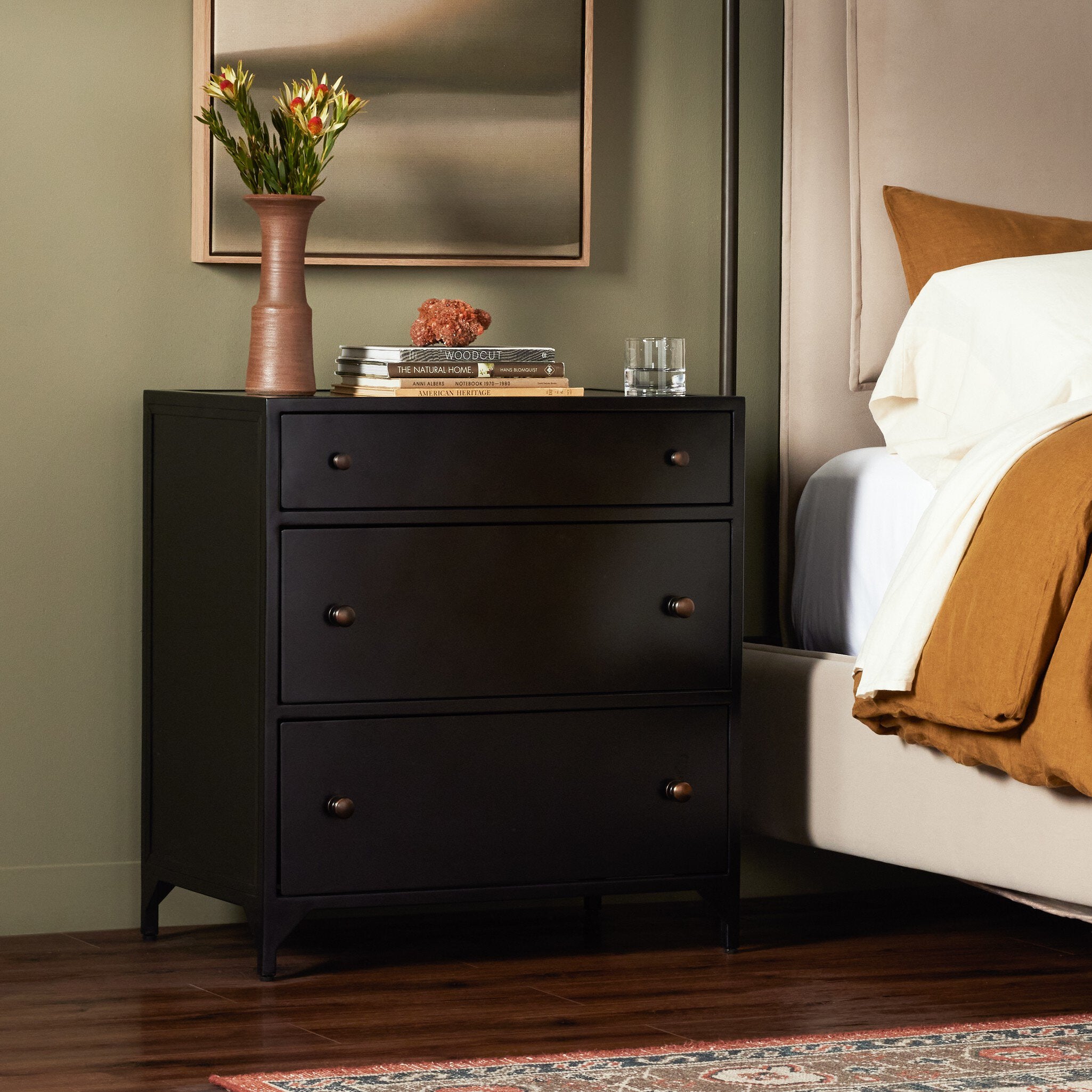 Black nightstand next to a bed with a vase and books on top in a bedroom setting. | Wildwood Home Co.