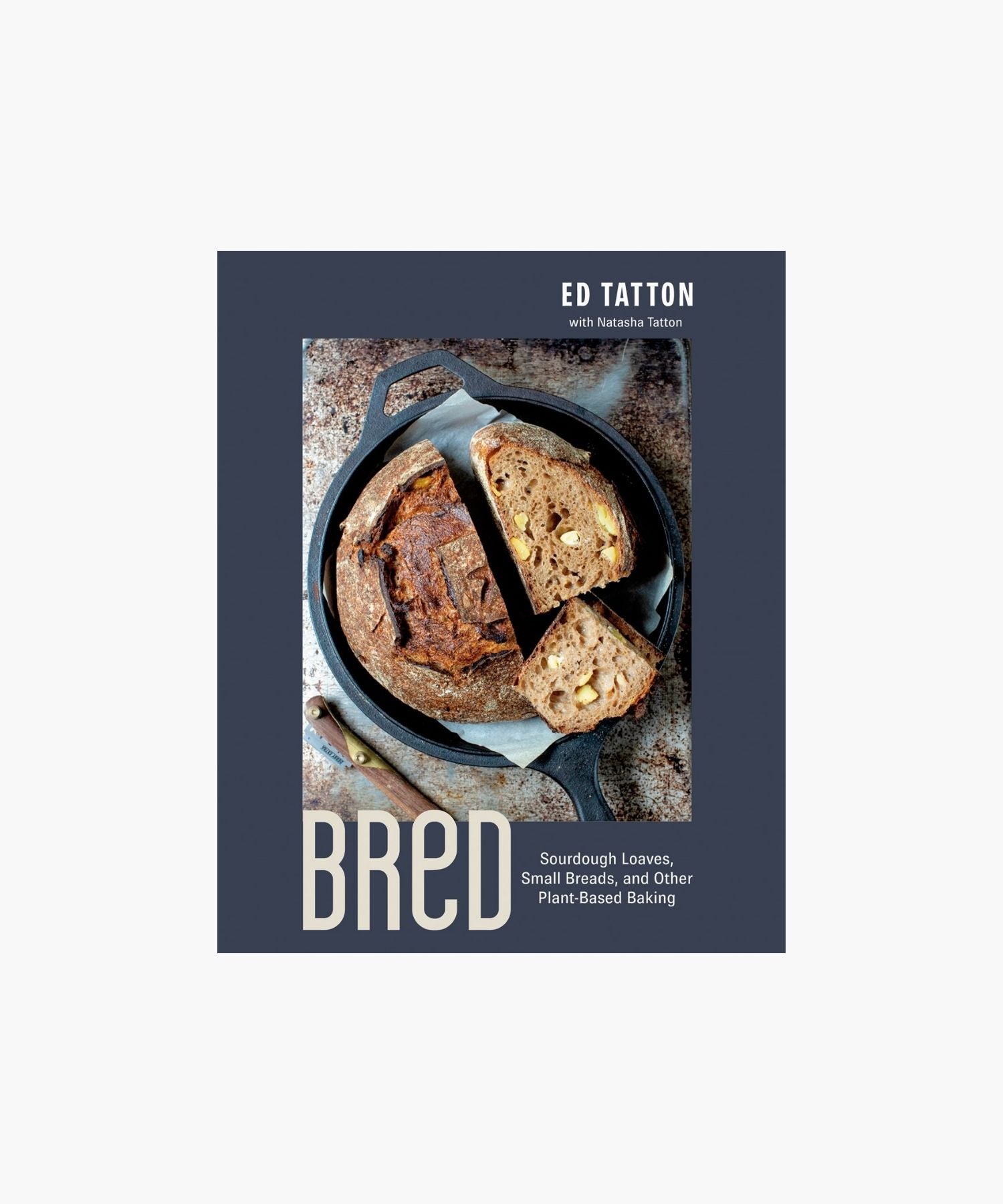 Cookbook cover titled "Bred: Sourdough Loaves, Small Breads, and other Plant-Based Baking" by Ed Tatton features a sliced, rustic loaf in a cast iron pan on a textured surface, conveying a cozy, artisanal feel. | Wildwood Home Co.