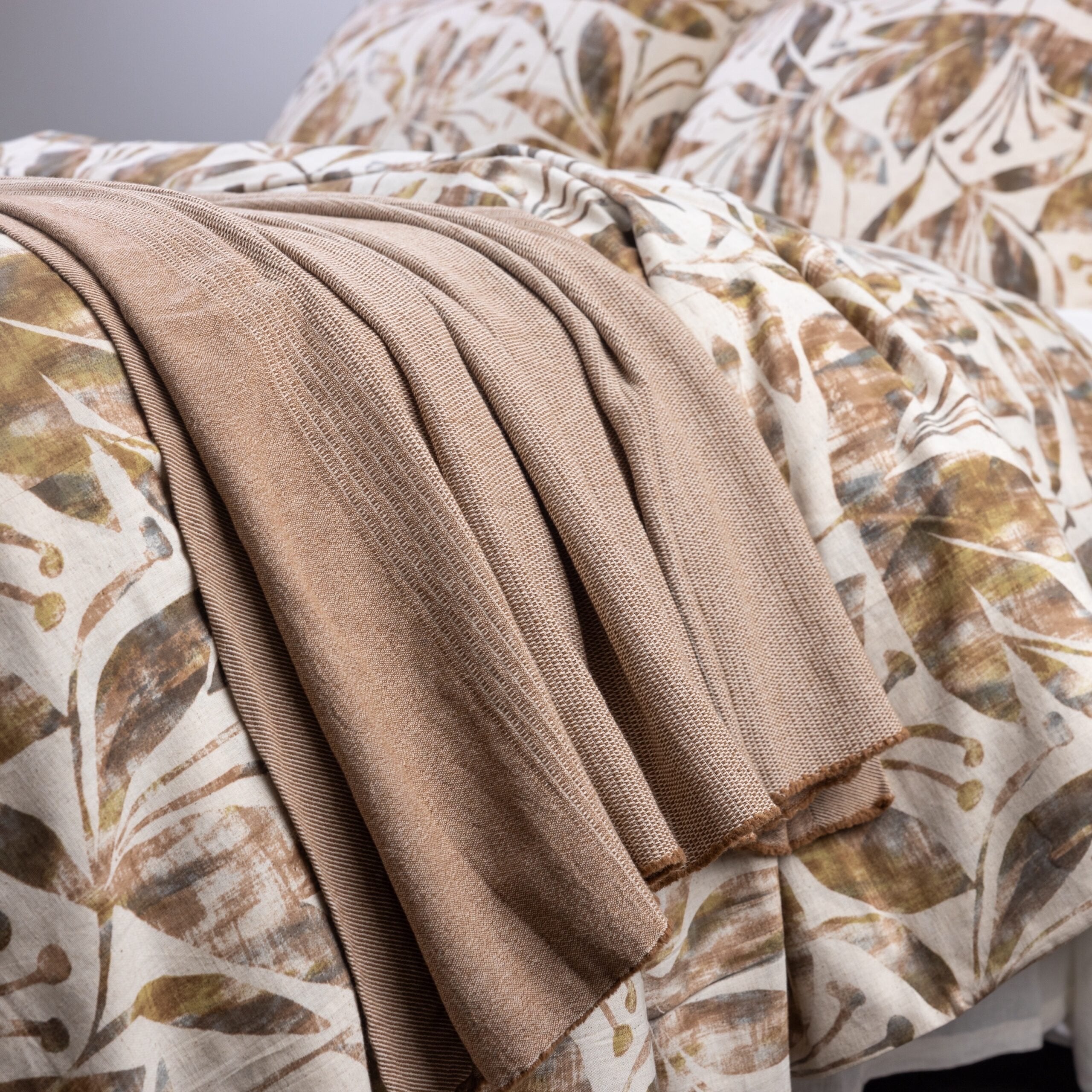 Burhan Coverlet casually draped across a printed duvet for a layered look, showcasing its camel hue and relaxed knit texture.