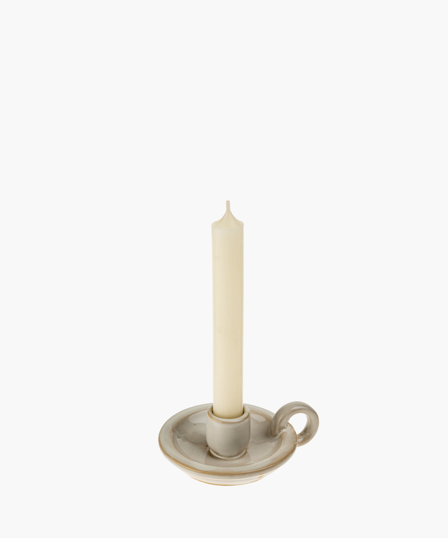 A cream-colored, unlit taper candle stands in a classic ceramic holder with a handle, evoking simplicity and elegance against a plain white background.