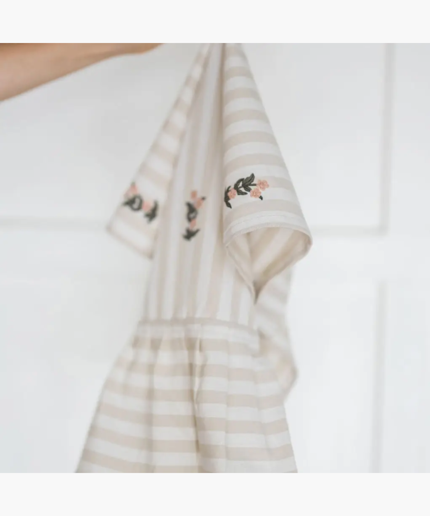 A beige striped kitchen towel featuring an embroidered floral motif in the center. The gathered ruffle adds an elegant touch. | Wildwood Home Co.