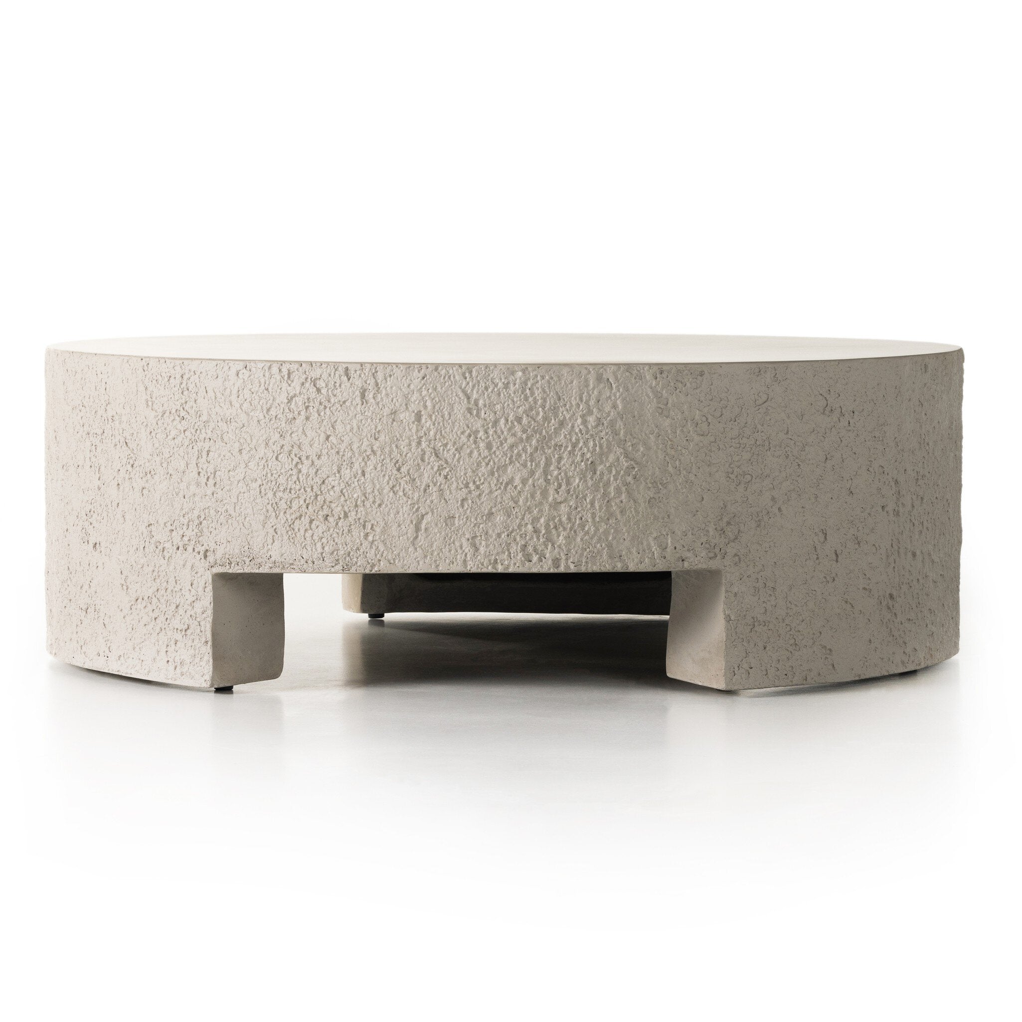 A round pumice concrete coffee table with a smooth top and cutout legs.