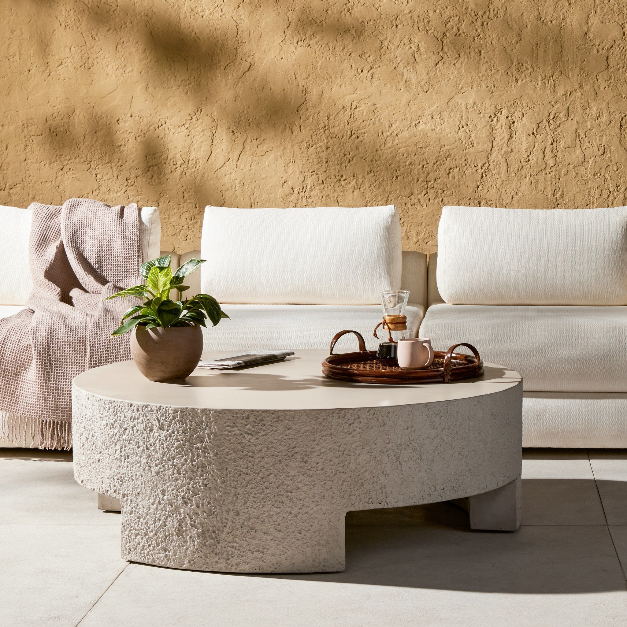 Round concrete coffee table with decorative items in front of a white sofa against a beige wall. | Wildwood Home Co.