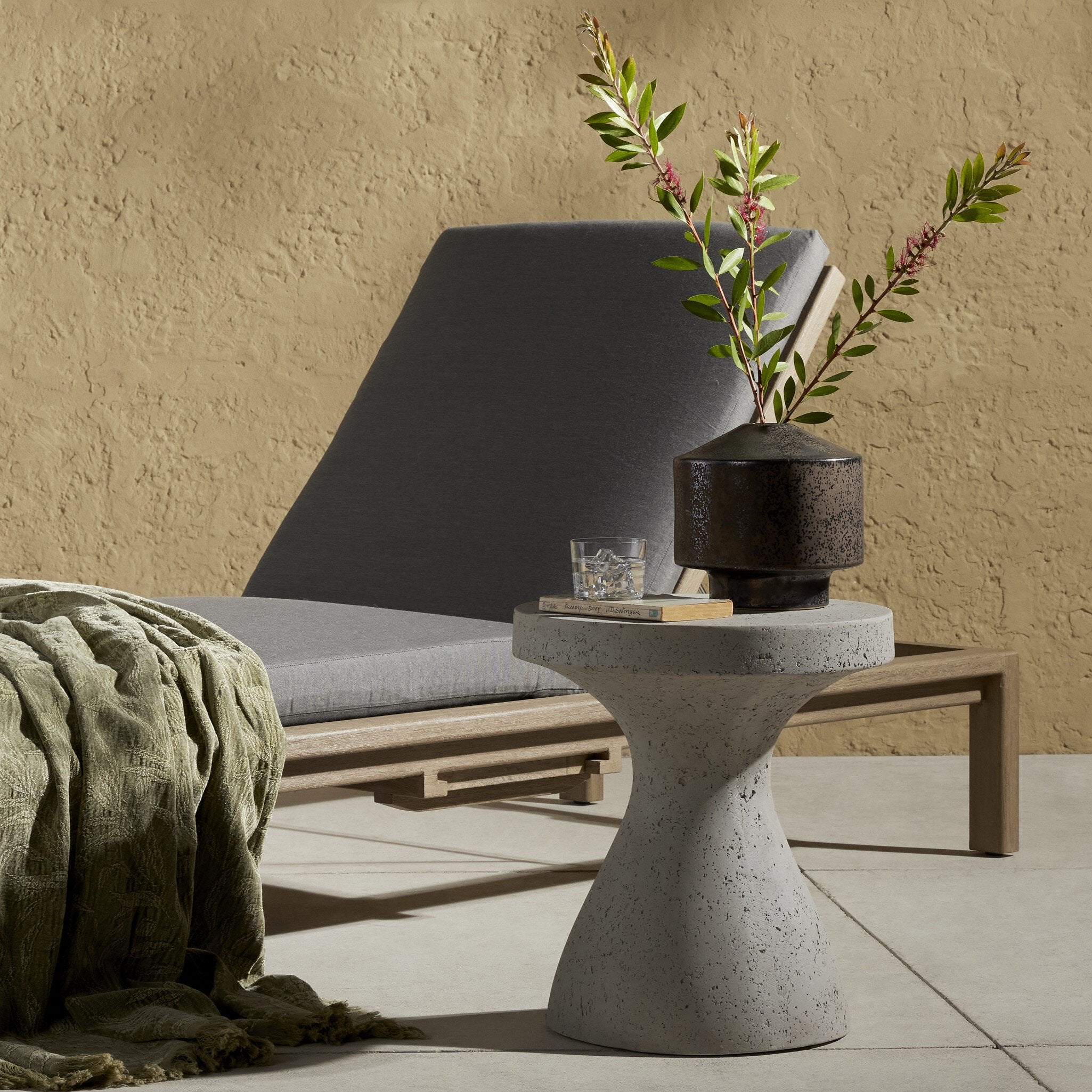 Outdoor setting with a concrete side table, gray lounge chair, and decorative plant. | Wildwood Home Co.