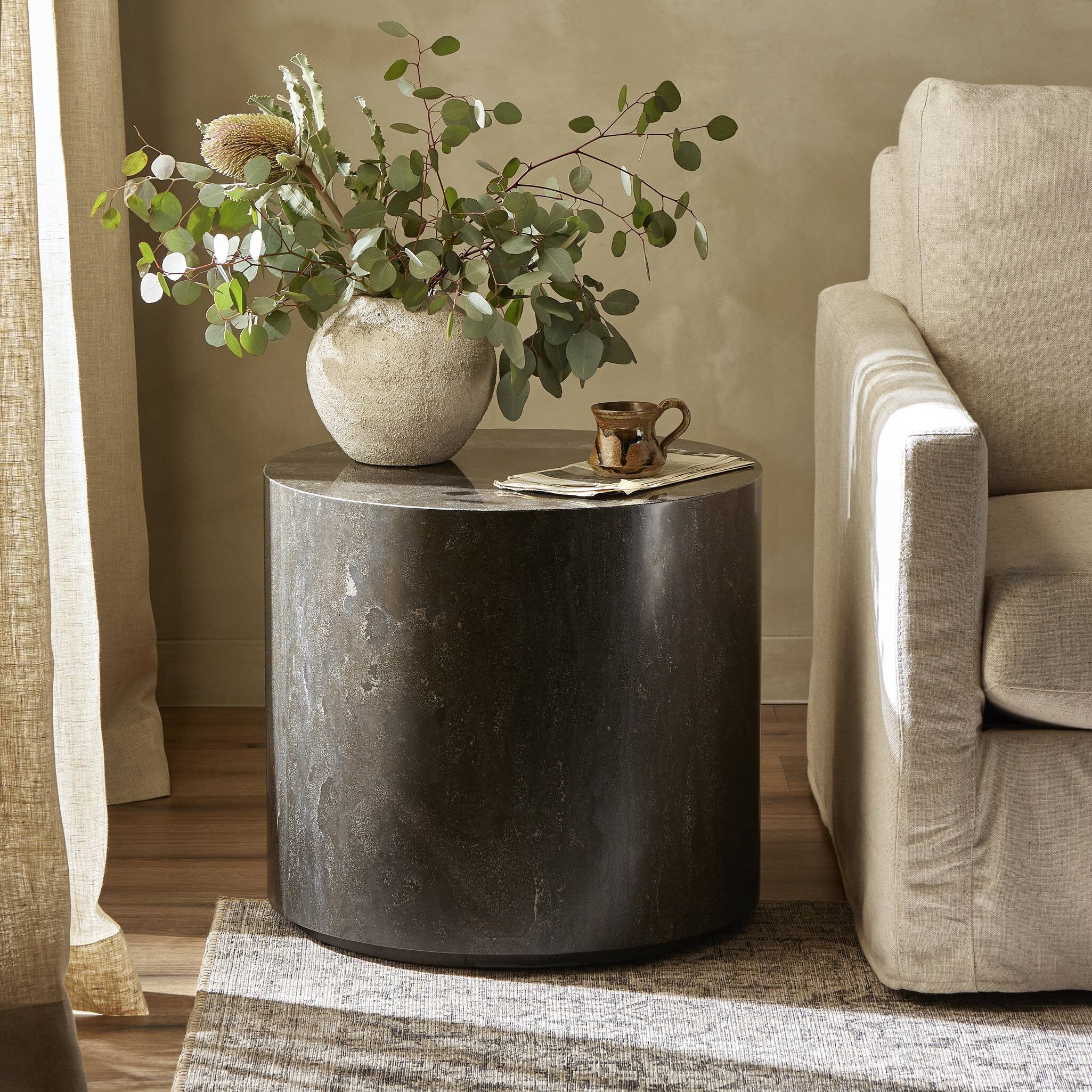 Round dark stone table with a vase of greenery and a mug in a living room setting. | Wildwood Home Co.